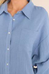 Close up view of this dress that features a collared neckline, functional buttons down the front, a front pocket on the left side of the bust, long sleeves with a cuff secured by a functional button, and two slits up the bottom hemline ending just below the knee.