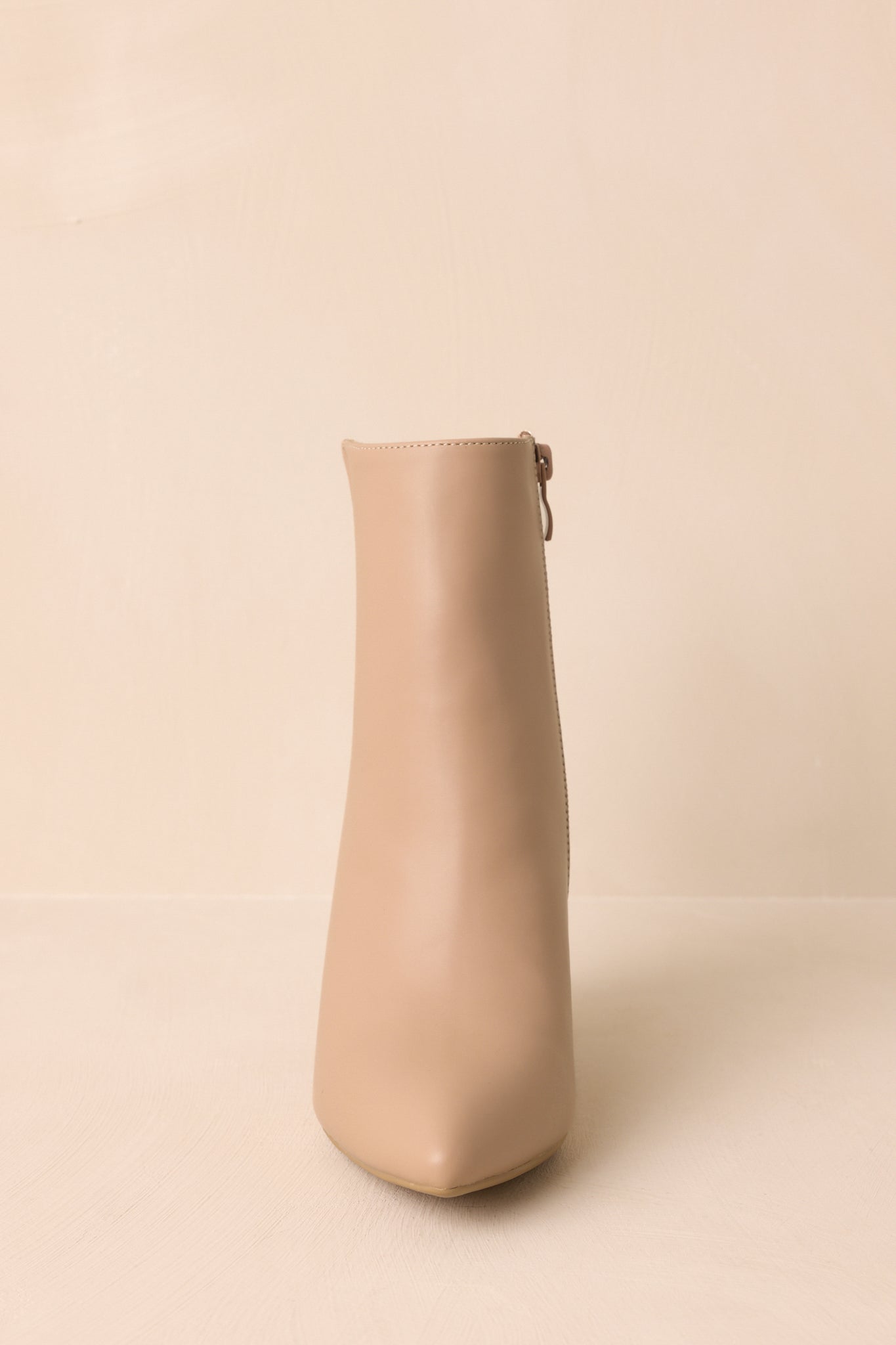 Straight-on front view of beige ankle boots with a polished, minimal design and pointed silhouette.