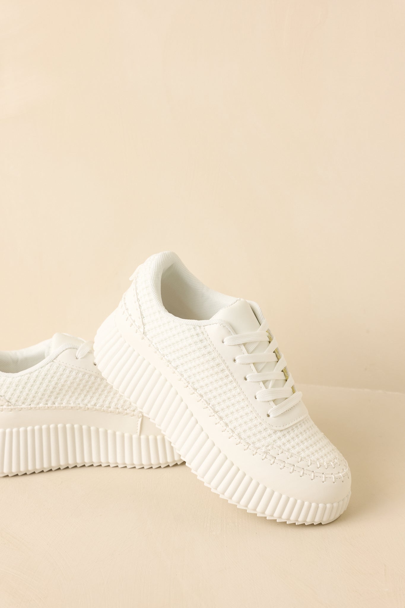 White sneakers focusing on the lace-up front and textured knit upper.