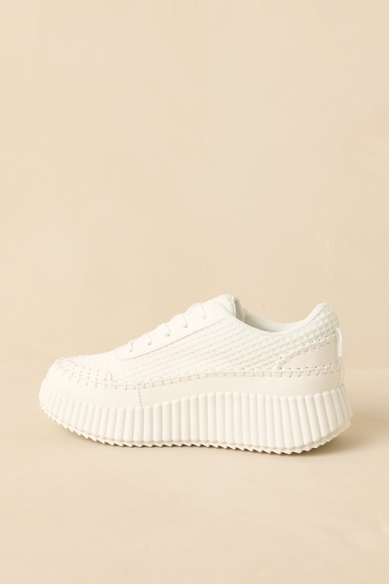 White lace-up sneakers displaying the side profile and ribbed outsole texture.