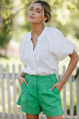  This white top features a v-neckline, a functional button front, embroidery throughout, and elastic cuffed puff sleeves.