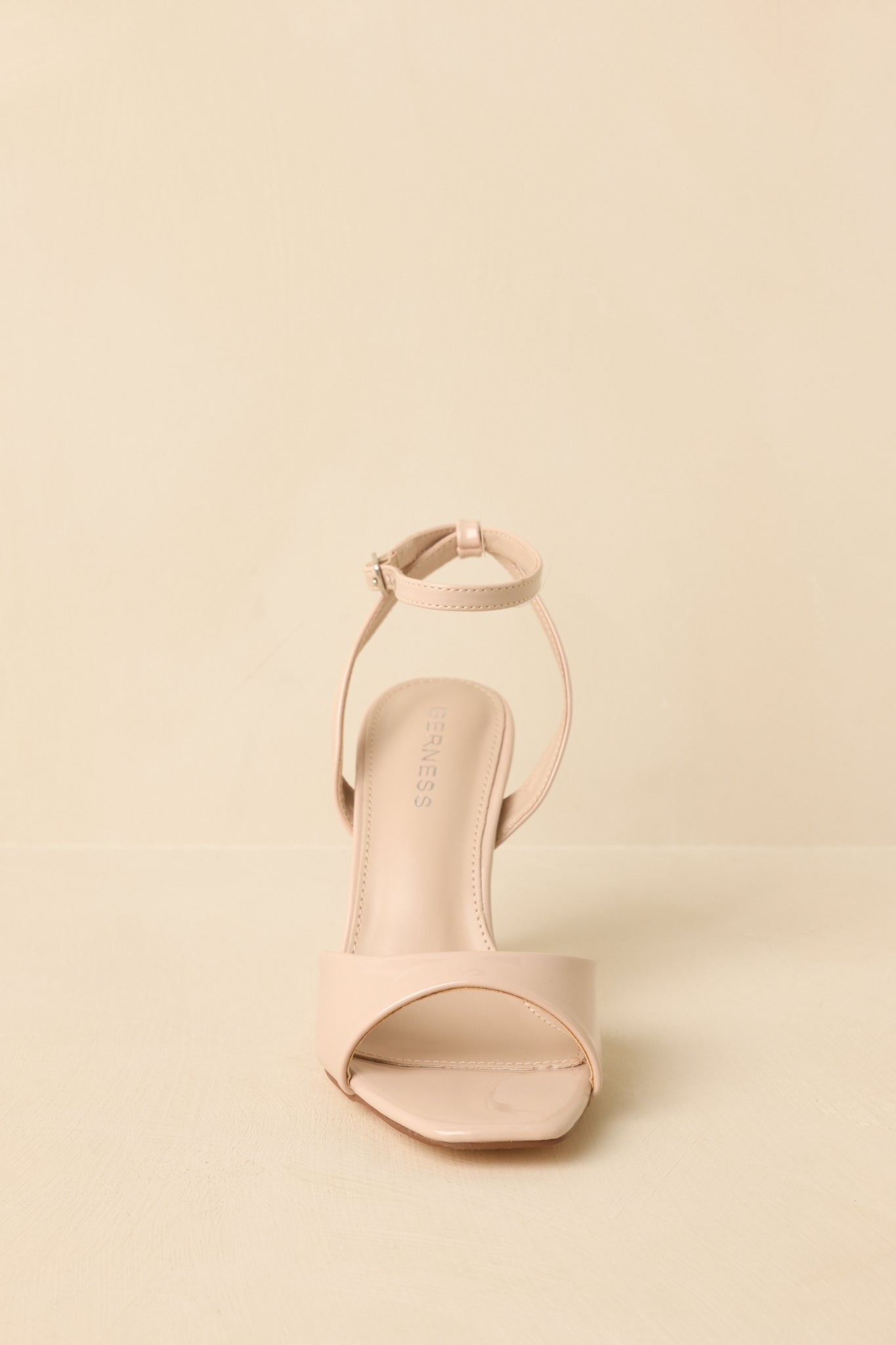 Front-facing view of beige open square-toe heels against a beige background highlighting the smooth front strap.