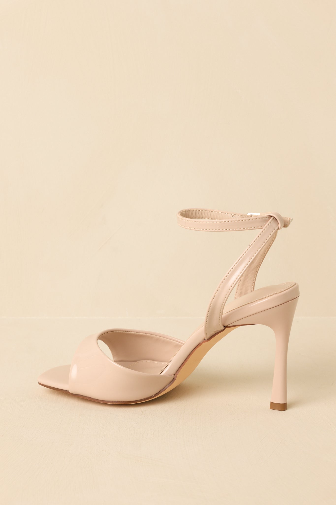 Angled rear-side view against a beige background focusing on the ankle strap and slim heel.