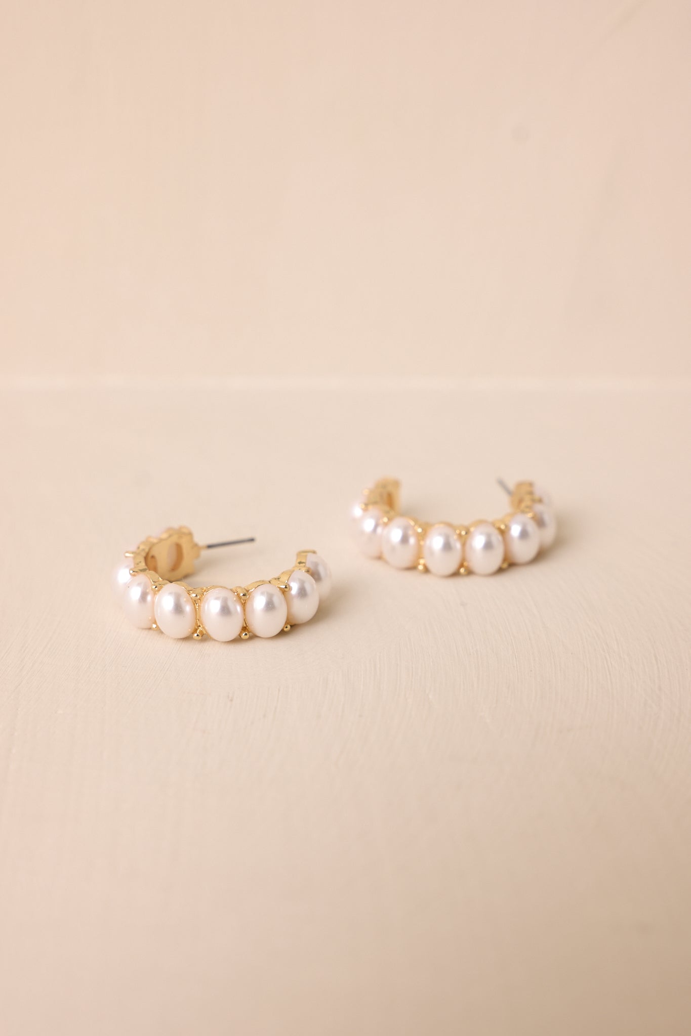 A close-up of gold and ivory earrings featuring an incomplete hoop design with medium-sized faux ivory pearls lining the outer hoop. The gold hardware and secure back postings complete the elegant look.