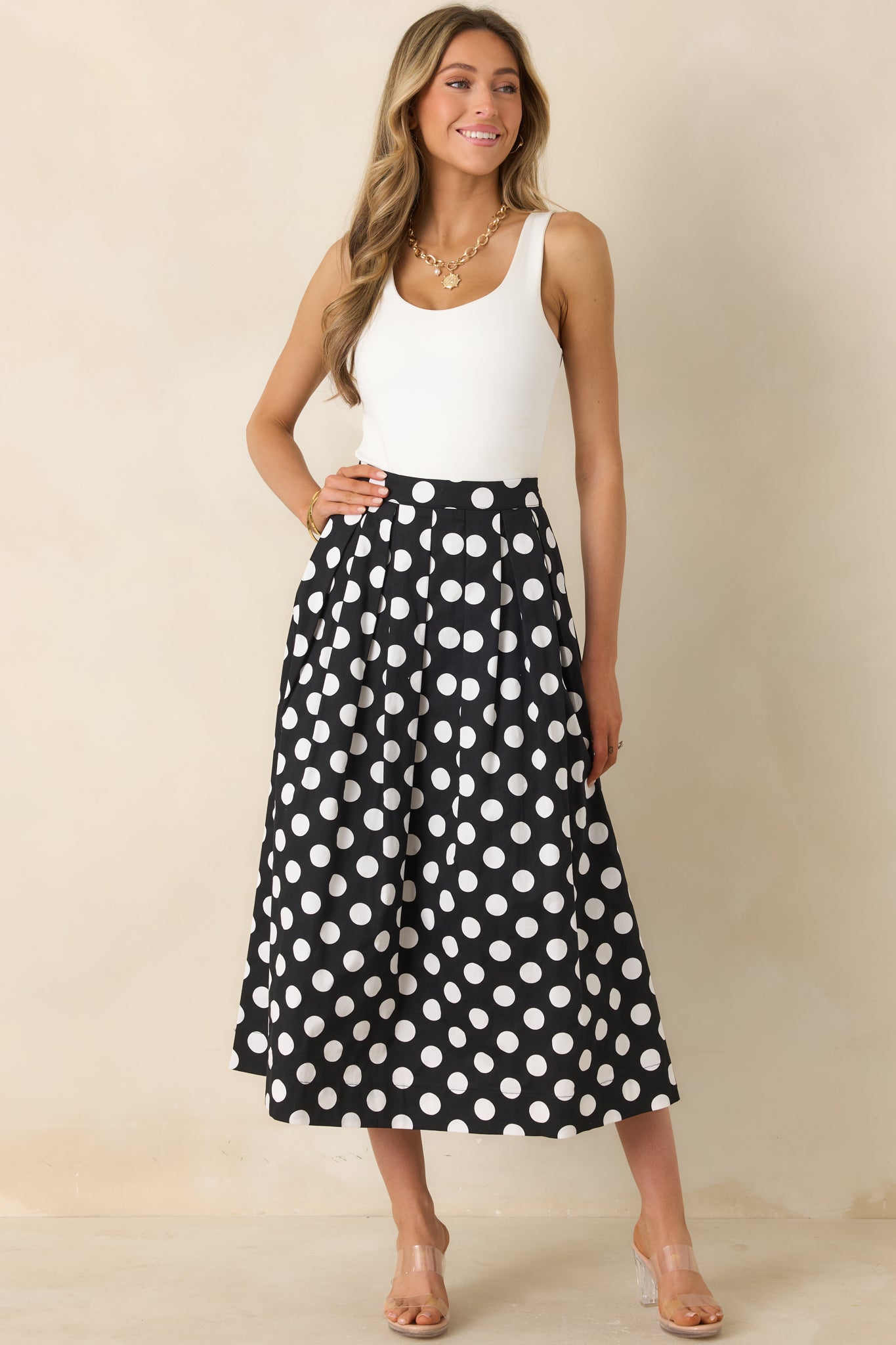 Full-length view of black and white polka dot maxi skirt featuring a high-rise waist and flowing pleated A-line silhouette.