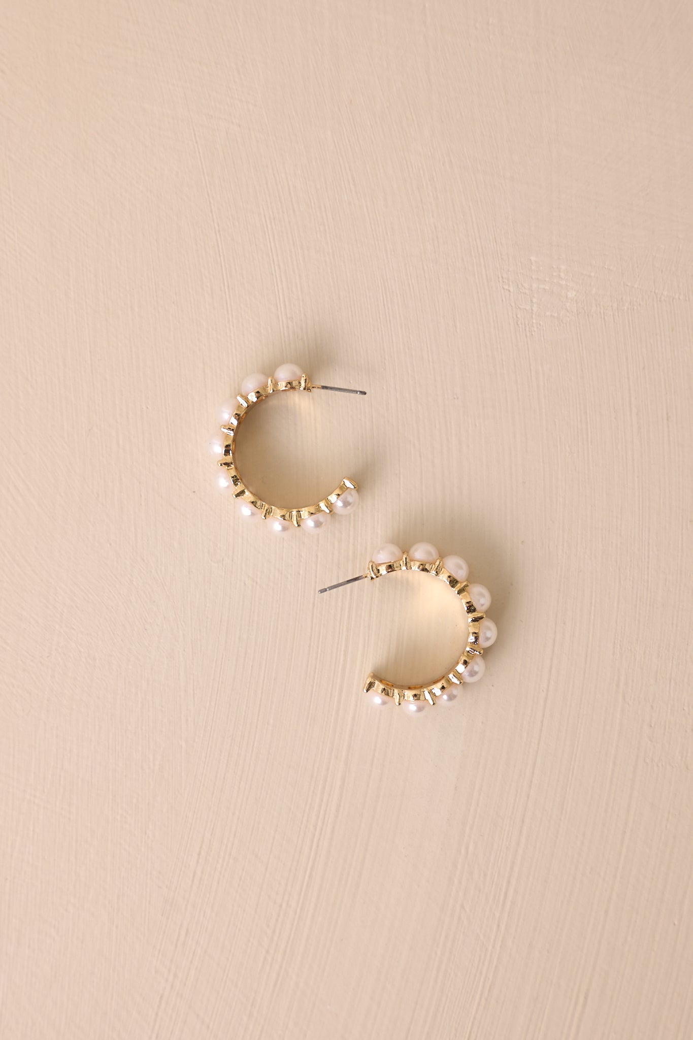 A detailed shot of the gold and ivory earrings, focusing on the medium-sized faux ivory pearls lining the incomplete hoop design, with the secure back postings visible and the gold hardware enhancing the overall style.