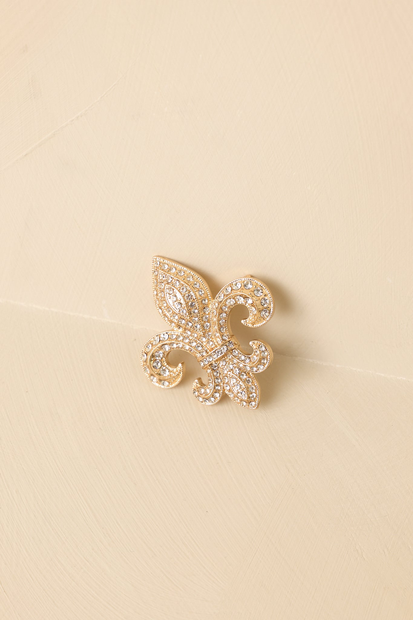 Zoomed-in image of the fleur-de-lis brooch focusing on the layered metal design and clear rhinestone accents.