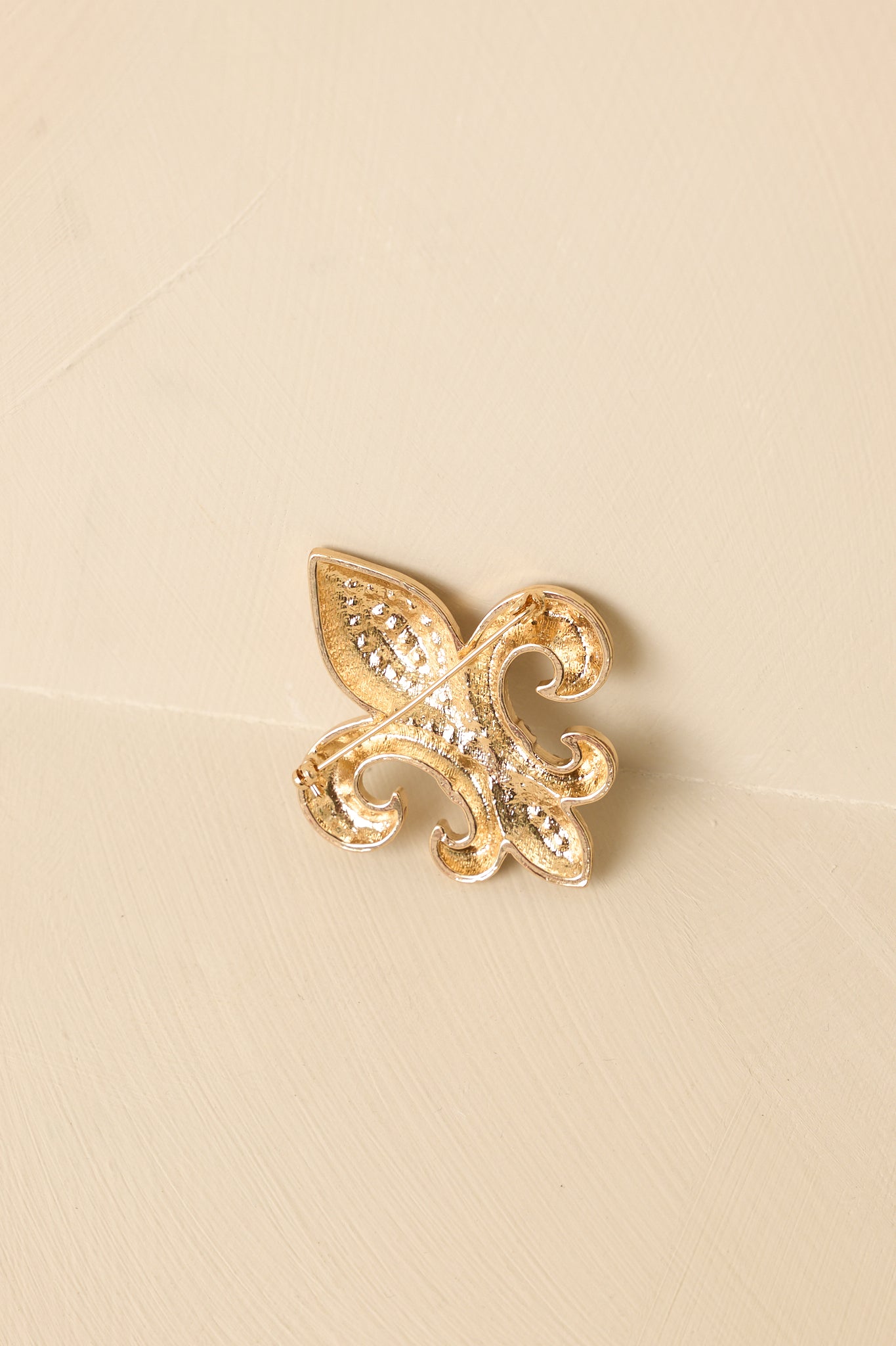 Back view of the gold fleur-de-lis brooch showing the secure pin-back closure and metal backing.