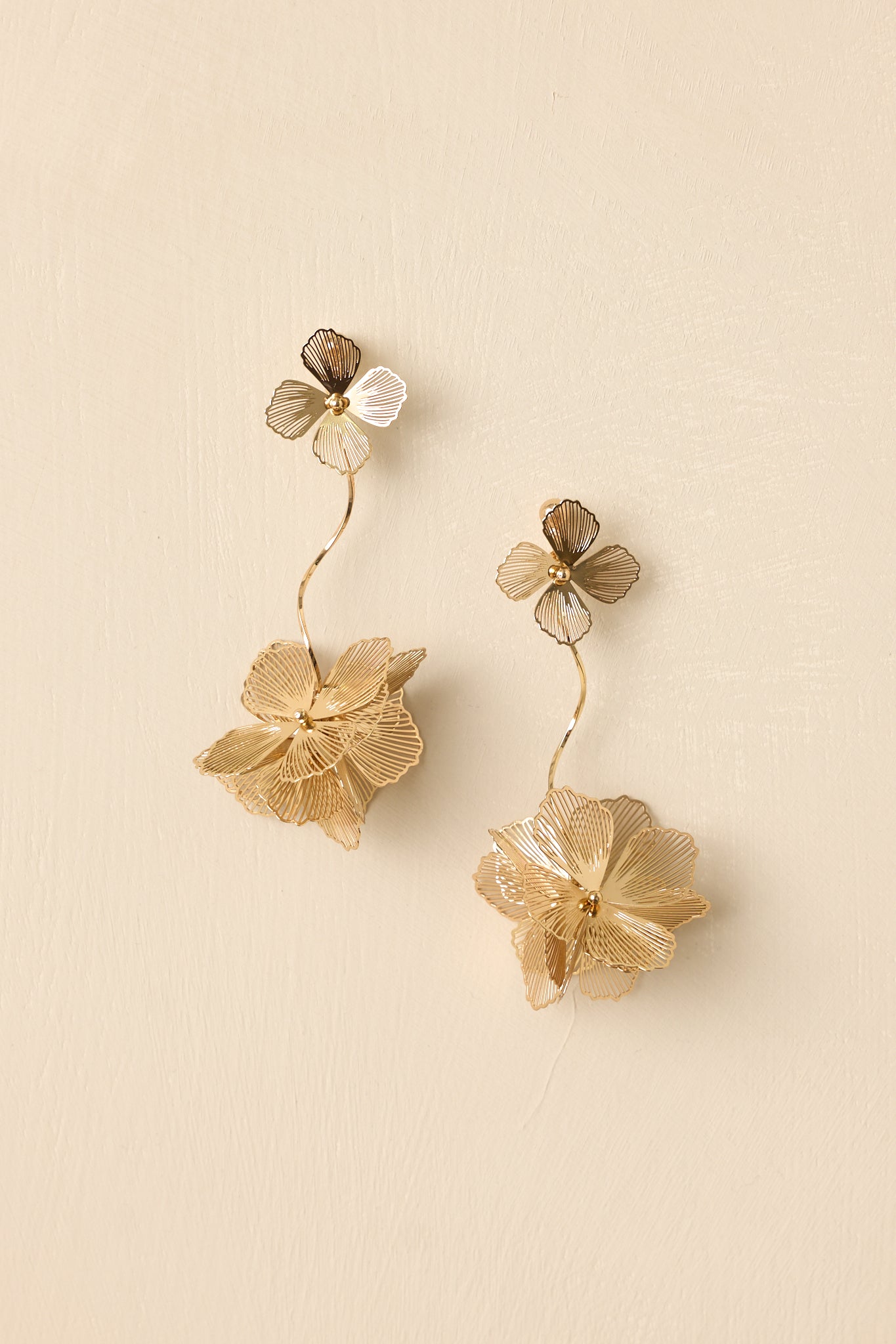 Detailed close-up of the gold-tone drop earrings focusing on the textured petals, curved stem, and dangling floral design.