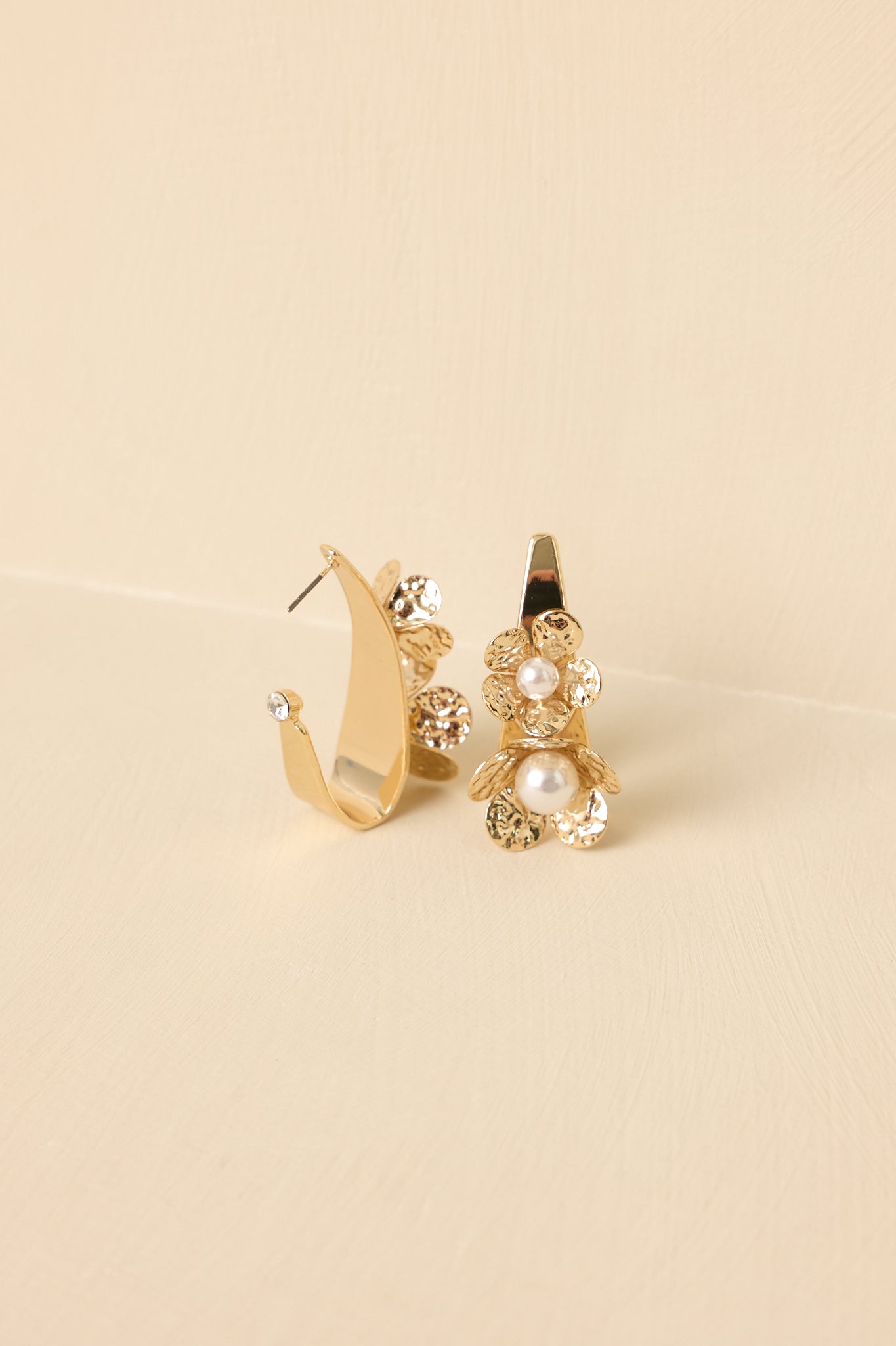 Angled view of the earrings against a beige backdrop highlighting the sculpted floral design and hoop silhouette.