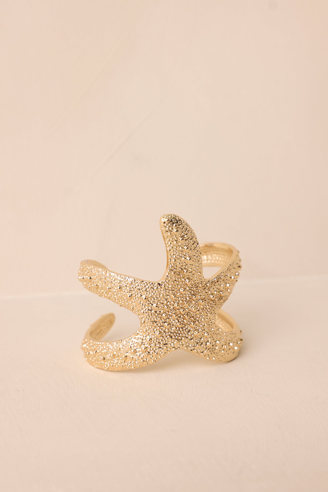 Close-up of gold starfish bracelet highlighting the textured beading, starfish shape, and open cuff structure.