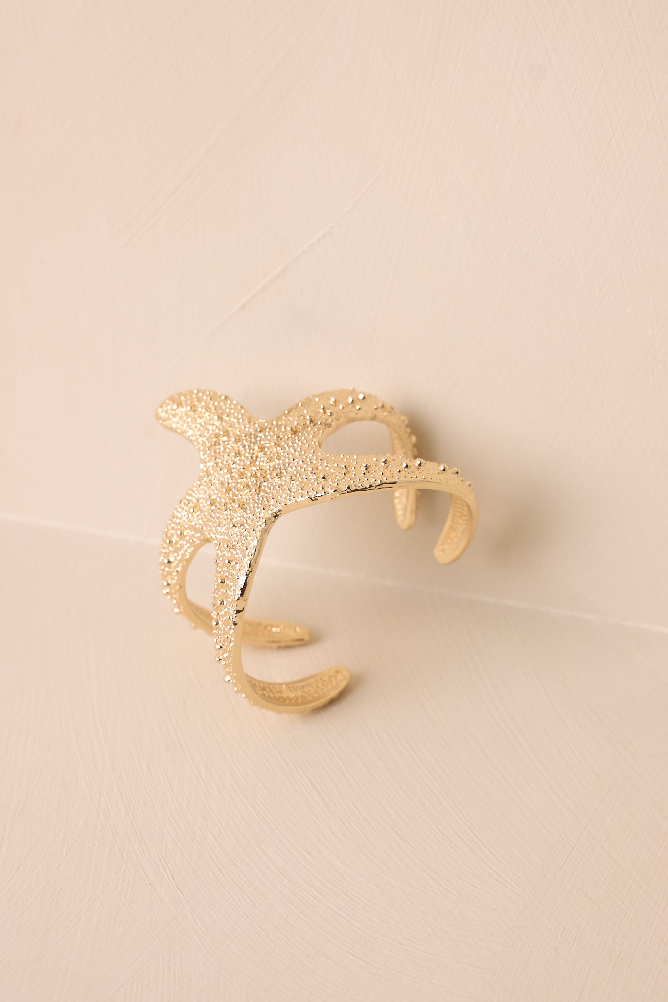 Angled view of gold bracelet against a neutral backdrop, emphasizing the sculpted starfish detail and polished beads.