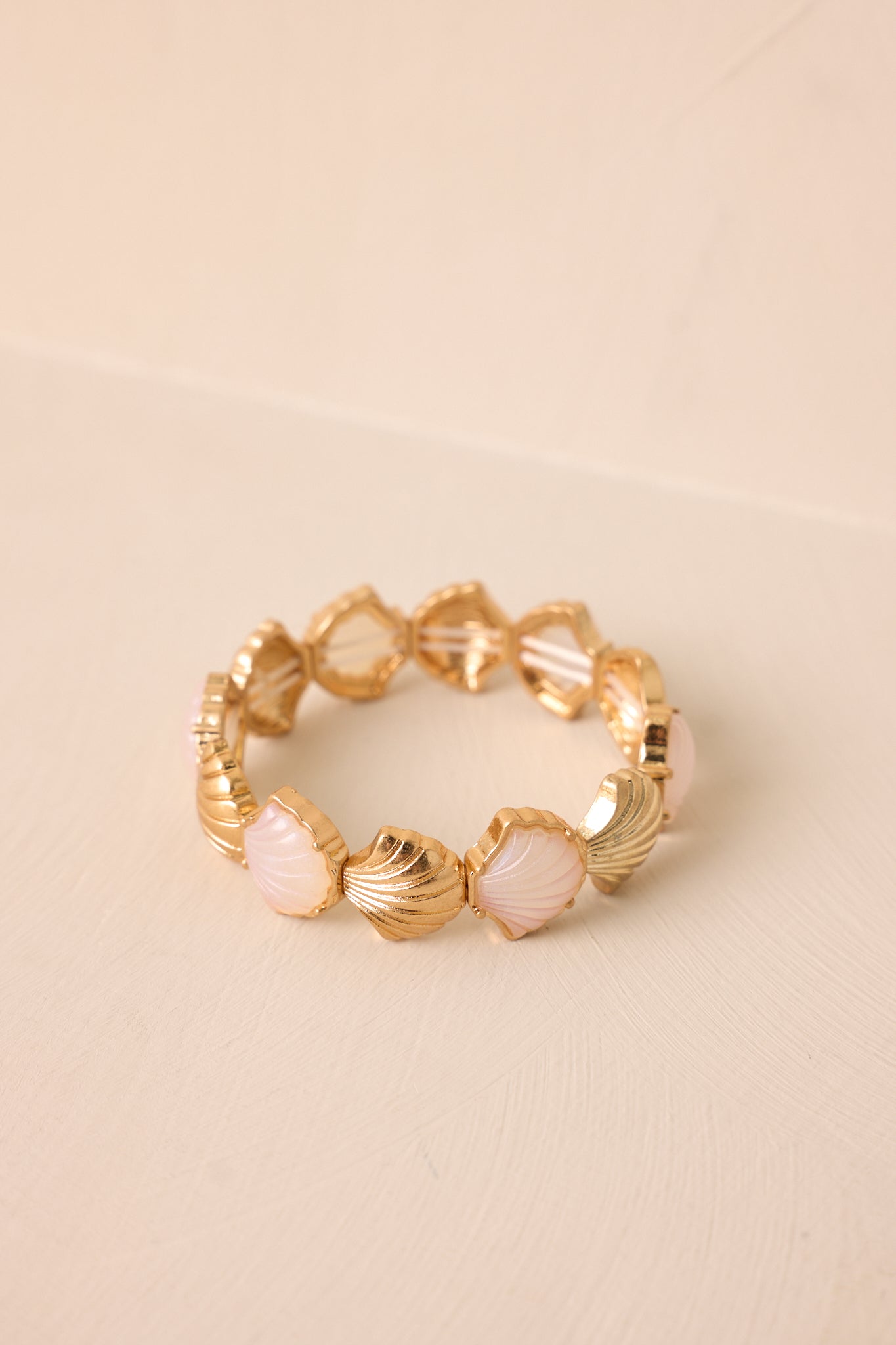 The gold and pearlescent seashell bracelet displayed against a neutral beige background, showcasing its full shape and elegant design.
