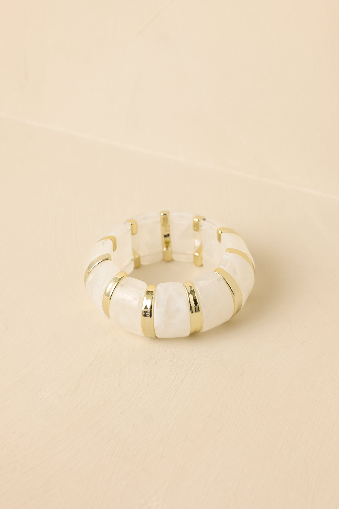 Detailed view of the marbled white and clear beads secured in smooth gold-tone settings on a stretch bracelet.