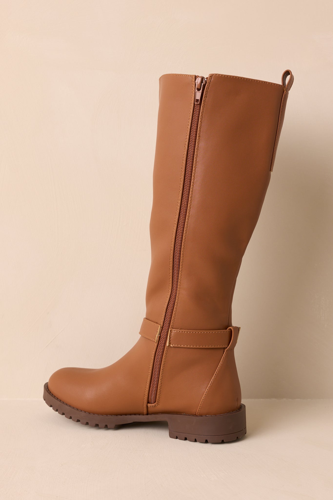 An angled back view of the caramel brown riding boots highlighting the pull tab, elastic panel, and structured shaft.