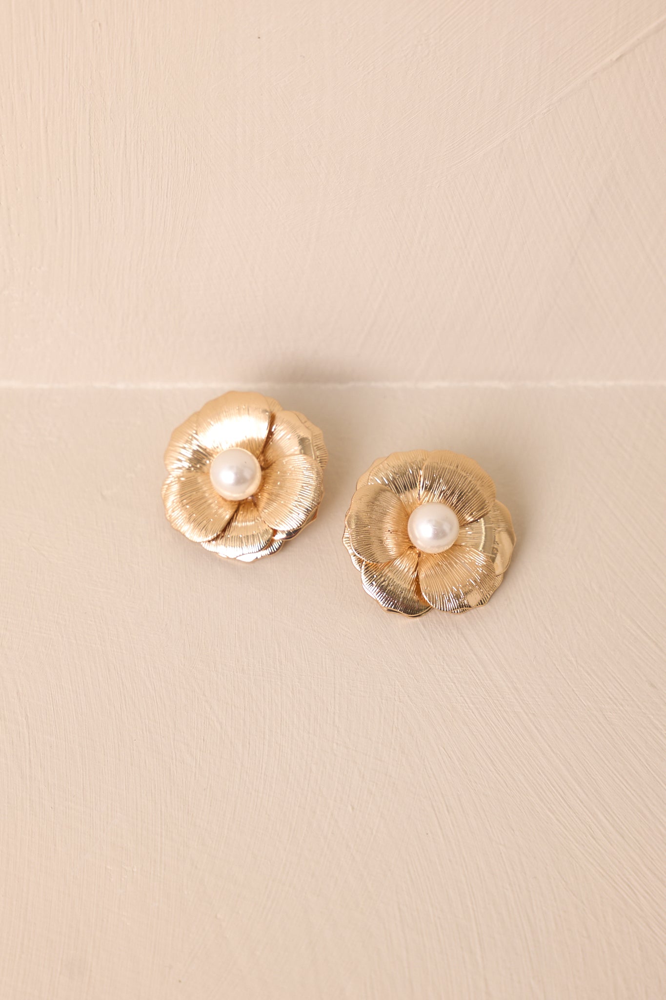 Close-up of the earring’s layered gold petals, ivory faux pearl center, and secure post backing construction.