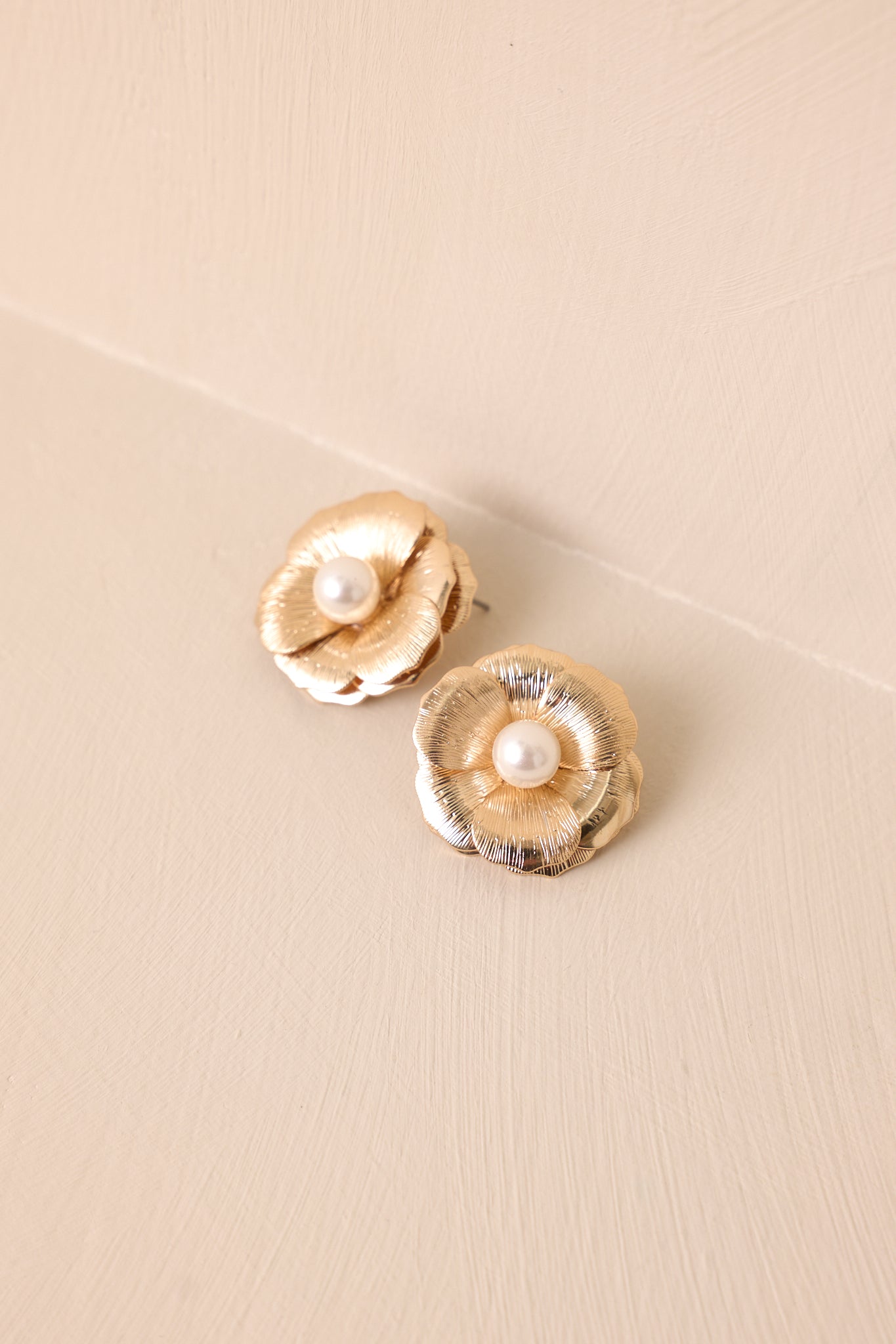 Top-down view of the flower earrings against a neutral beige surface, emphasizing the gold hardware and post backing.