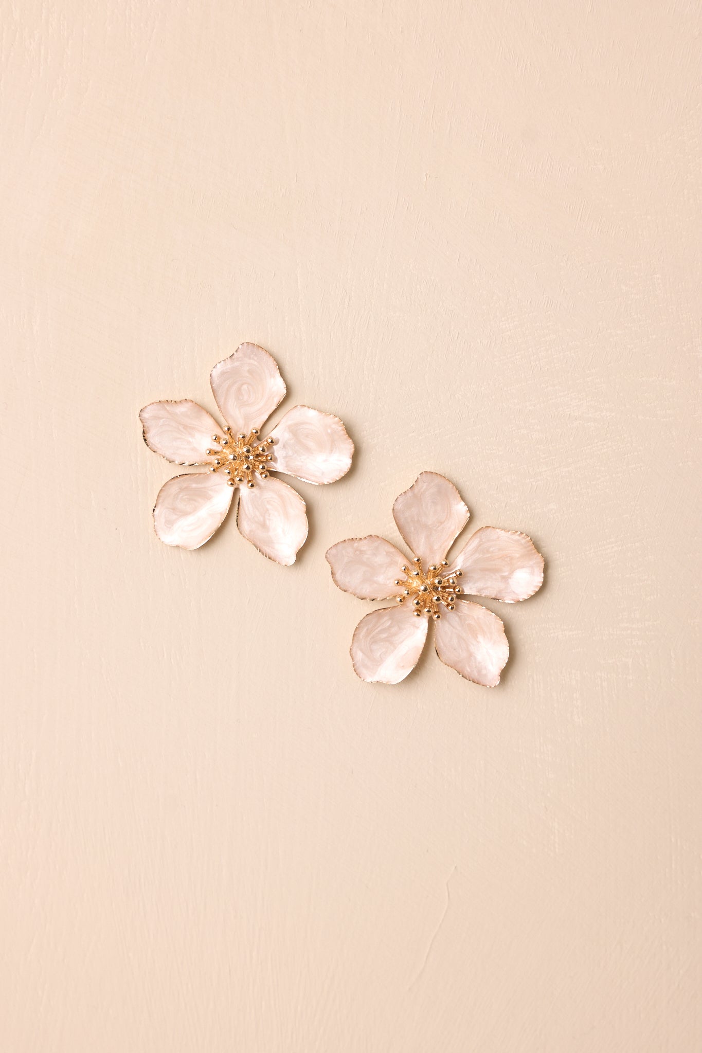 Flat lay of the earrings on a beige background displaying the full floral shape, gold hardware, and secure post backings.
