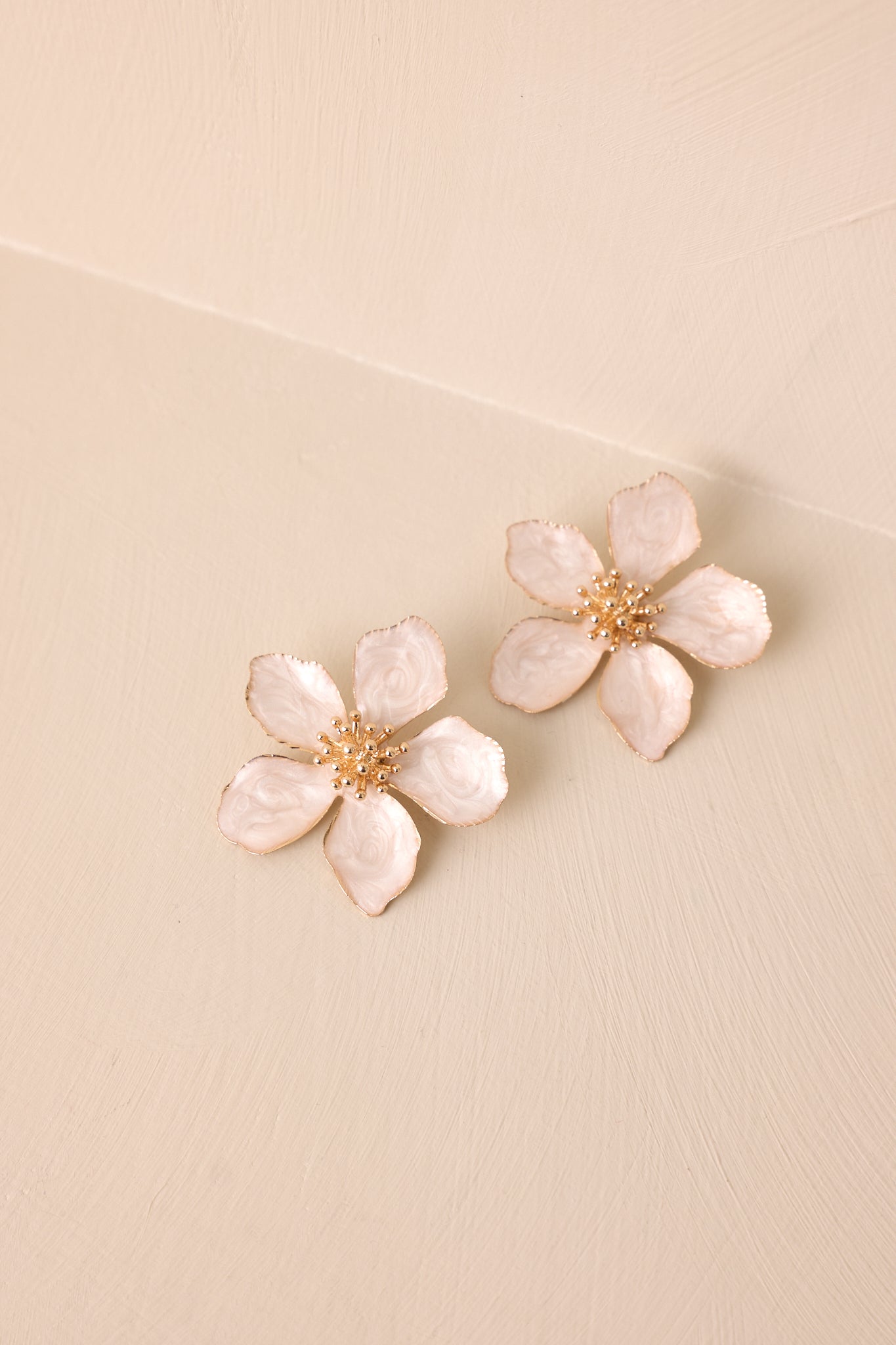 Angled overhead shot on a beige surface emphasizing the contrast between the pearlescent ivory petals and the textured gold center.