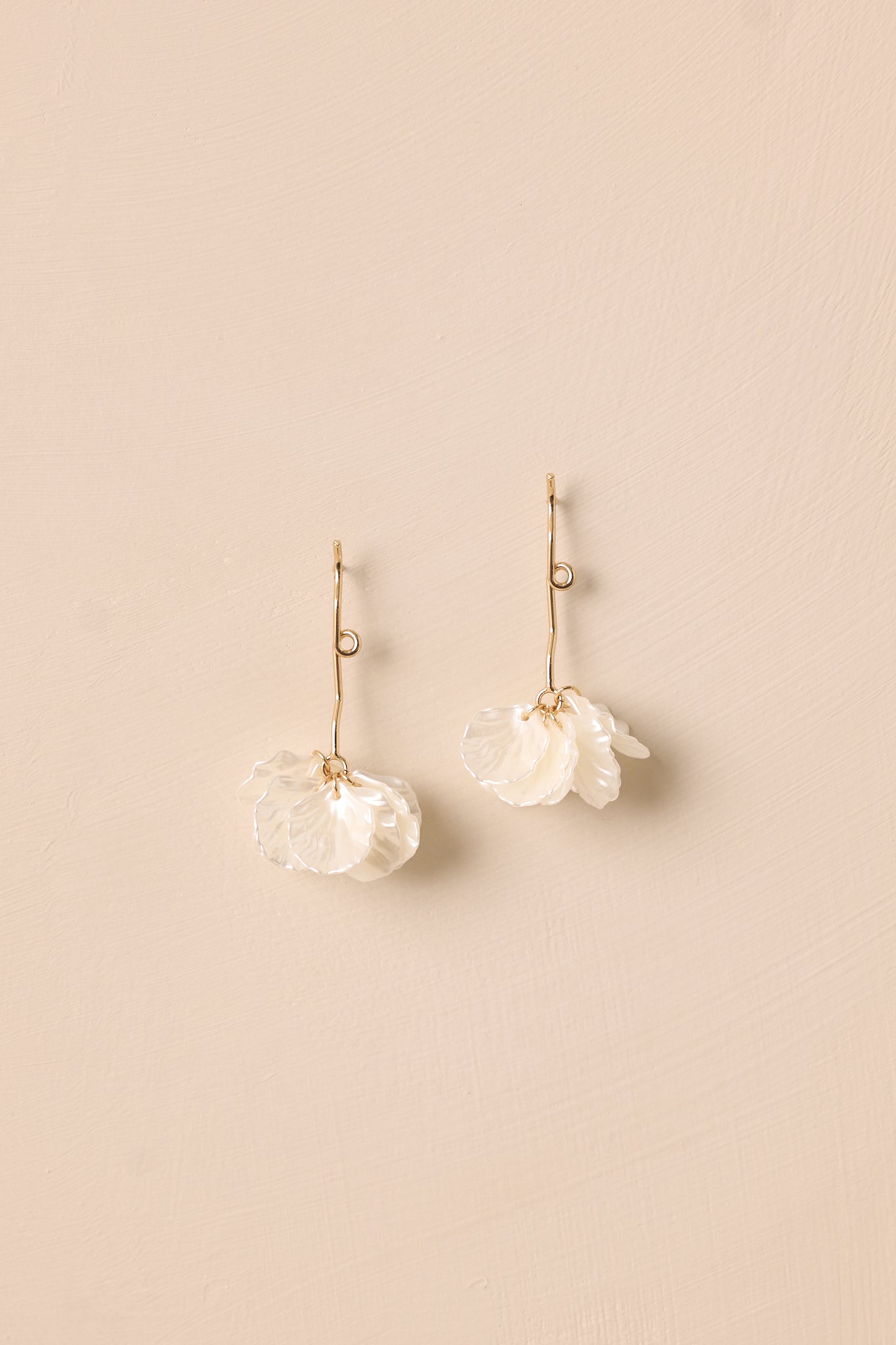 Another angle of the earrings against a beige background, emphasizing the long gold strand with one loop and the elegant arrangement of white leaf petals at the bottom.