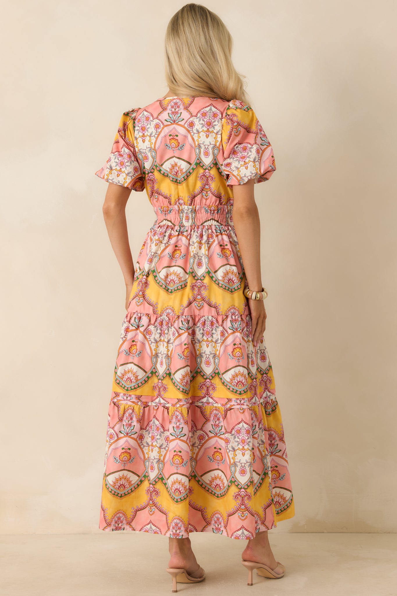 Pink and marigold cotton midi dress from the back, featuring short bubble sleeves, a comfortable elastic waist, and a flowing tiered skirt with continuous print coverage.