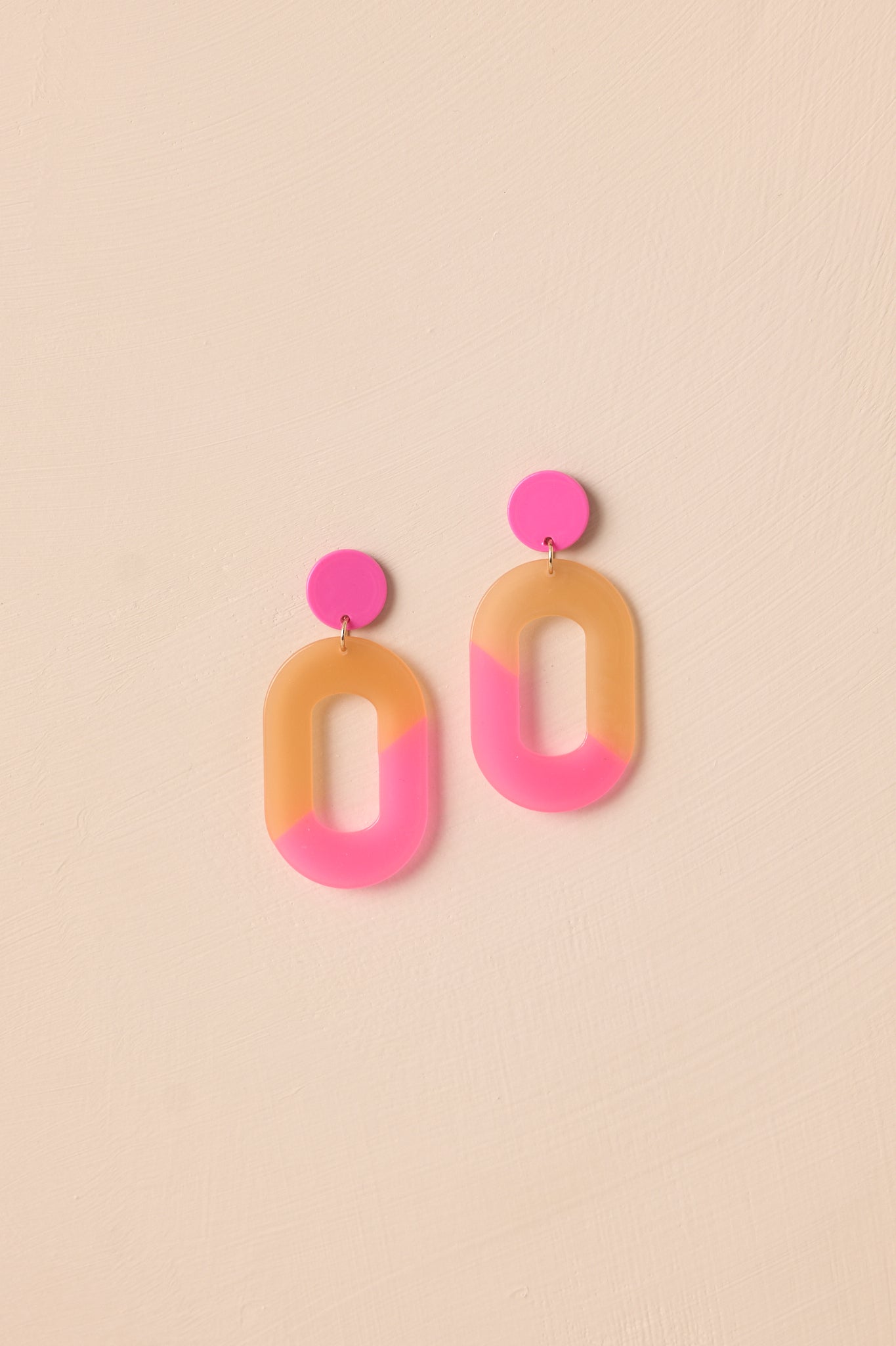 The pink and peach acrylic earrings displayed against a neutral beige background, showcasing their modern ombre design.