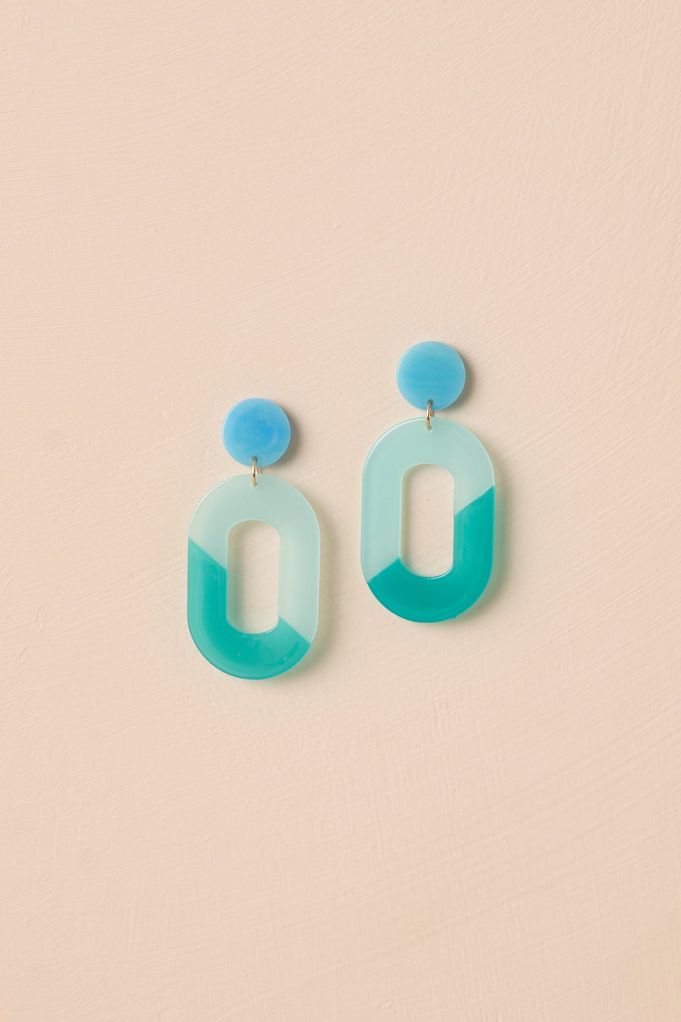 The blue and teal acrylic earrings displayed against a neutral beige background, showcasing their modern ombre design.