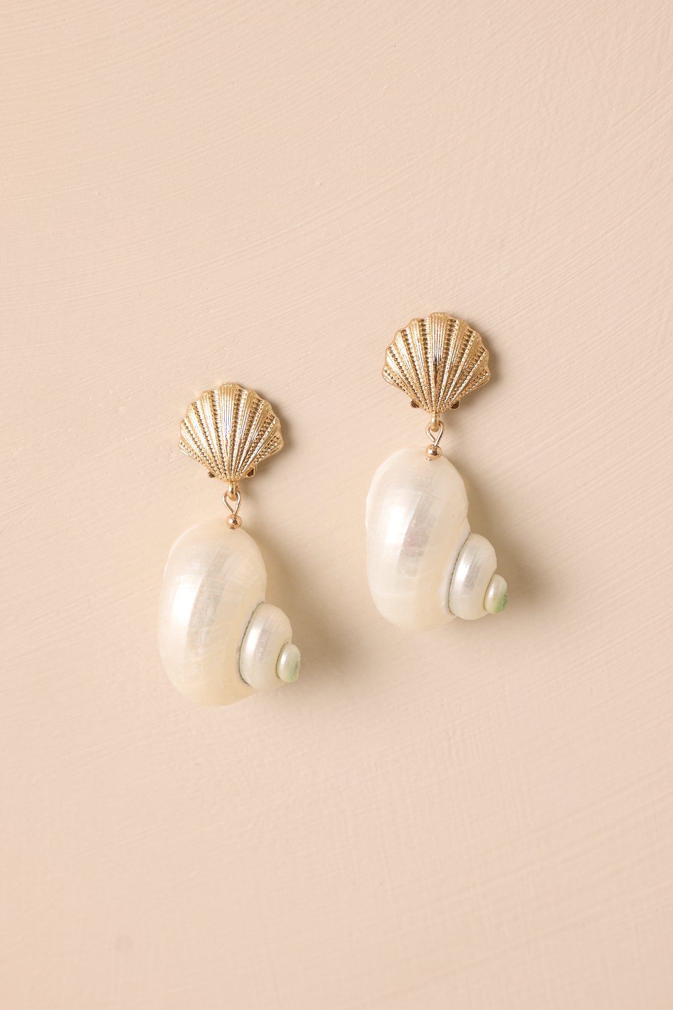 Gold earrings on a beige background, showcasing the textured scallop shell stud and the large white pearlescent tun shell with green accent.
