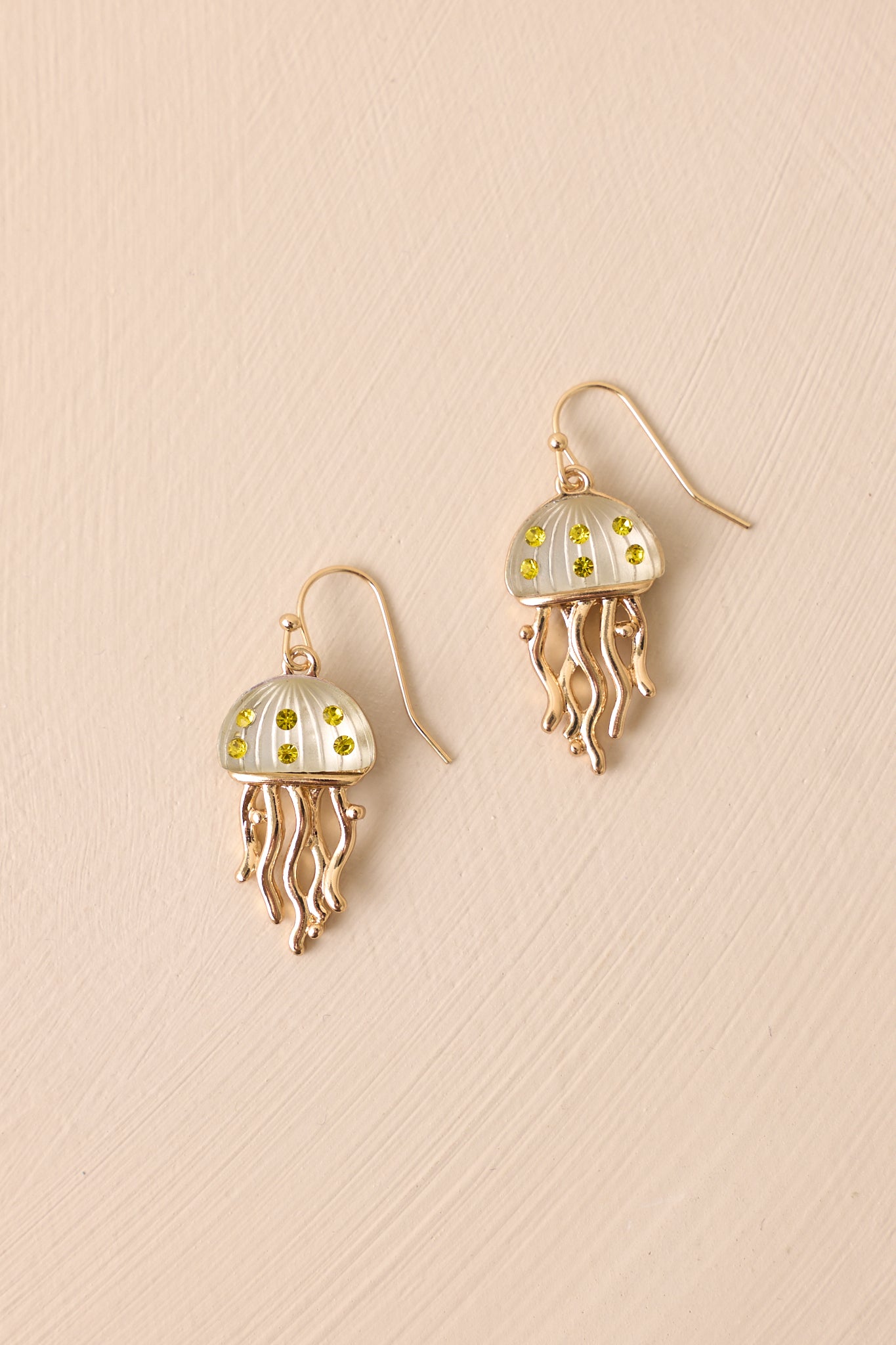 A focused view of the green jellyfish earrings, showcasing the intricate green rhinestones on the jellyfish body, the gold tentacles, and the gold fish hook wire post.