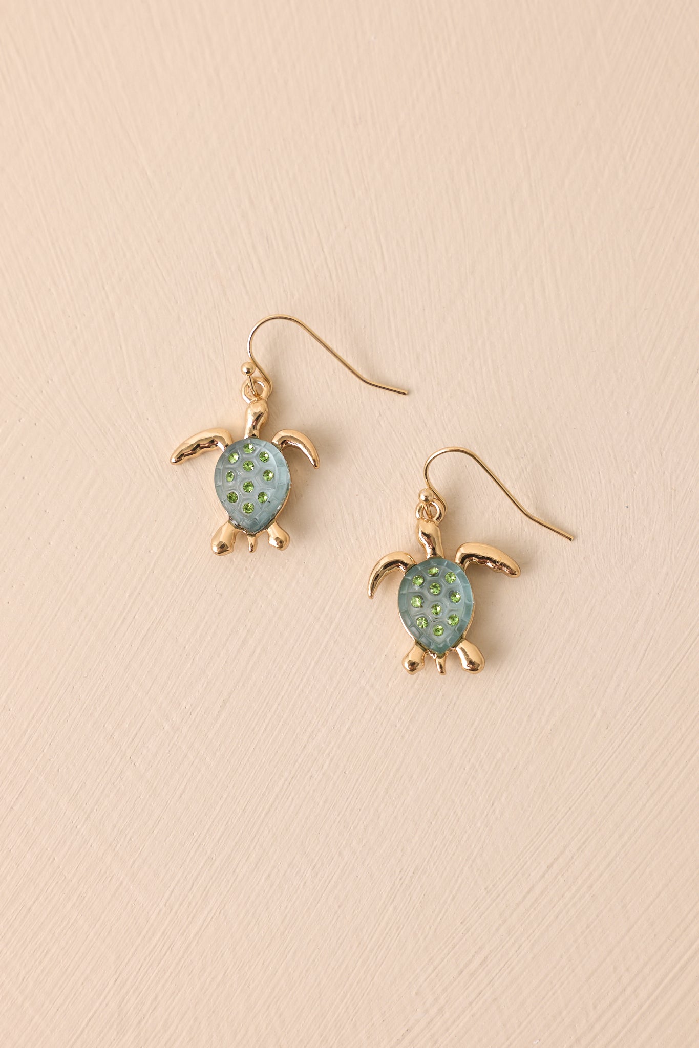A stunning pair of gold turtle dangle earrings emphasizing the gold detailing, light blue shell, and green rhinestones.