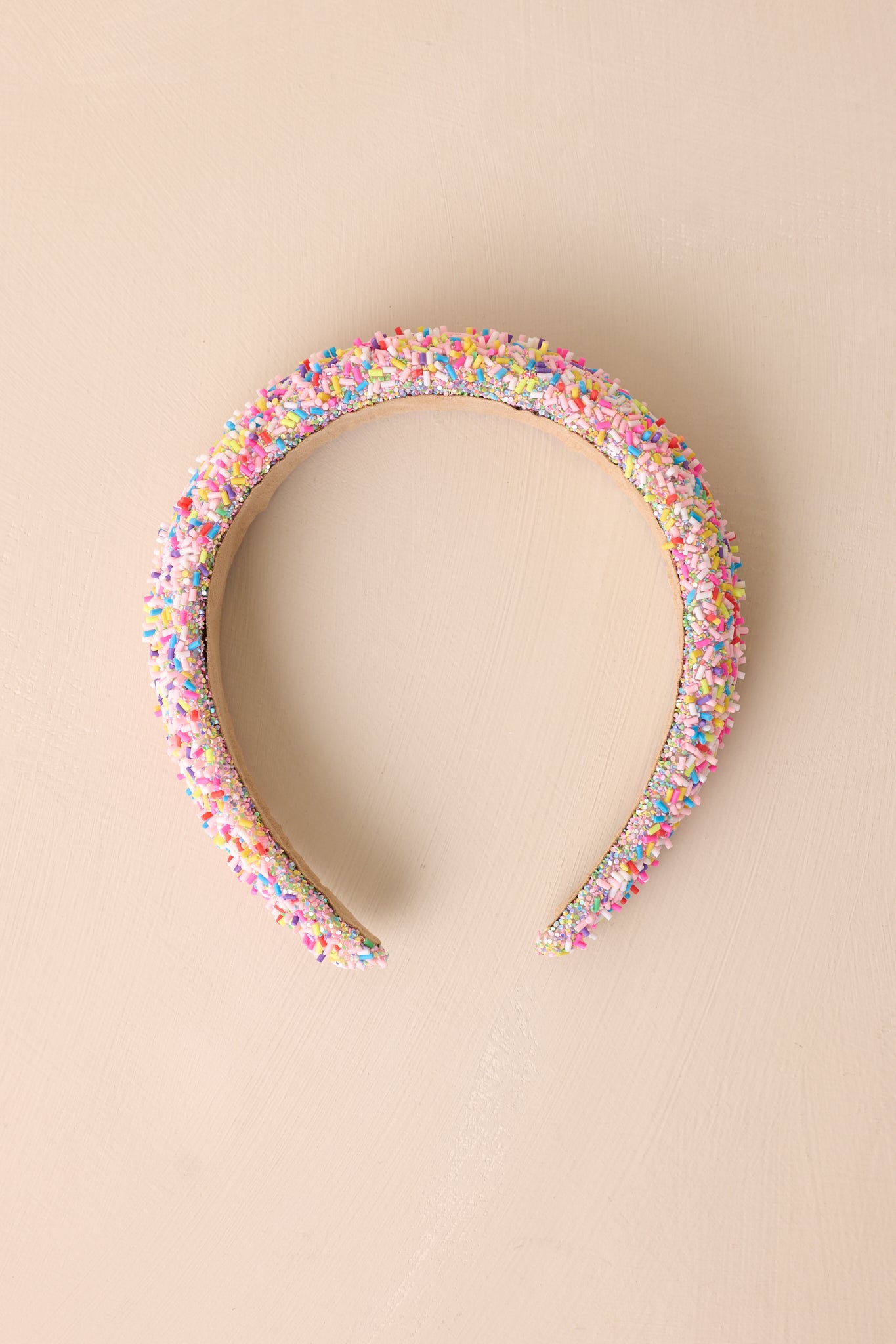 The headband displayed on a neutral beige background, showcasing the full design with its colorful sprinkles, glitter, and soft tan interior.