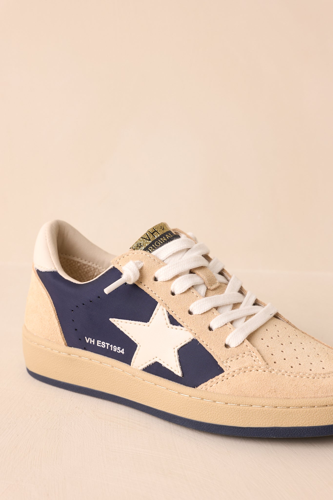 Close-up of the gold logo tongue tab, laces, and perforated suede texture across the upper.