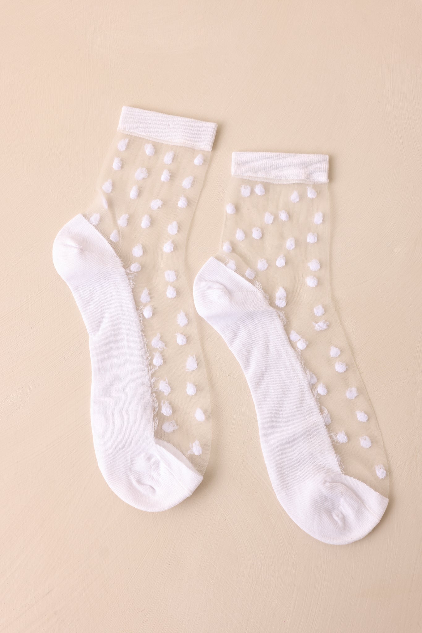 The white sheer socks displayed against a beige background, emphasizing the soft scrunched top, polka dot details, and elegant sheer design.