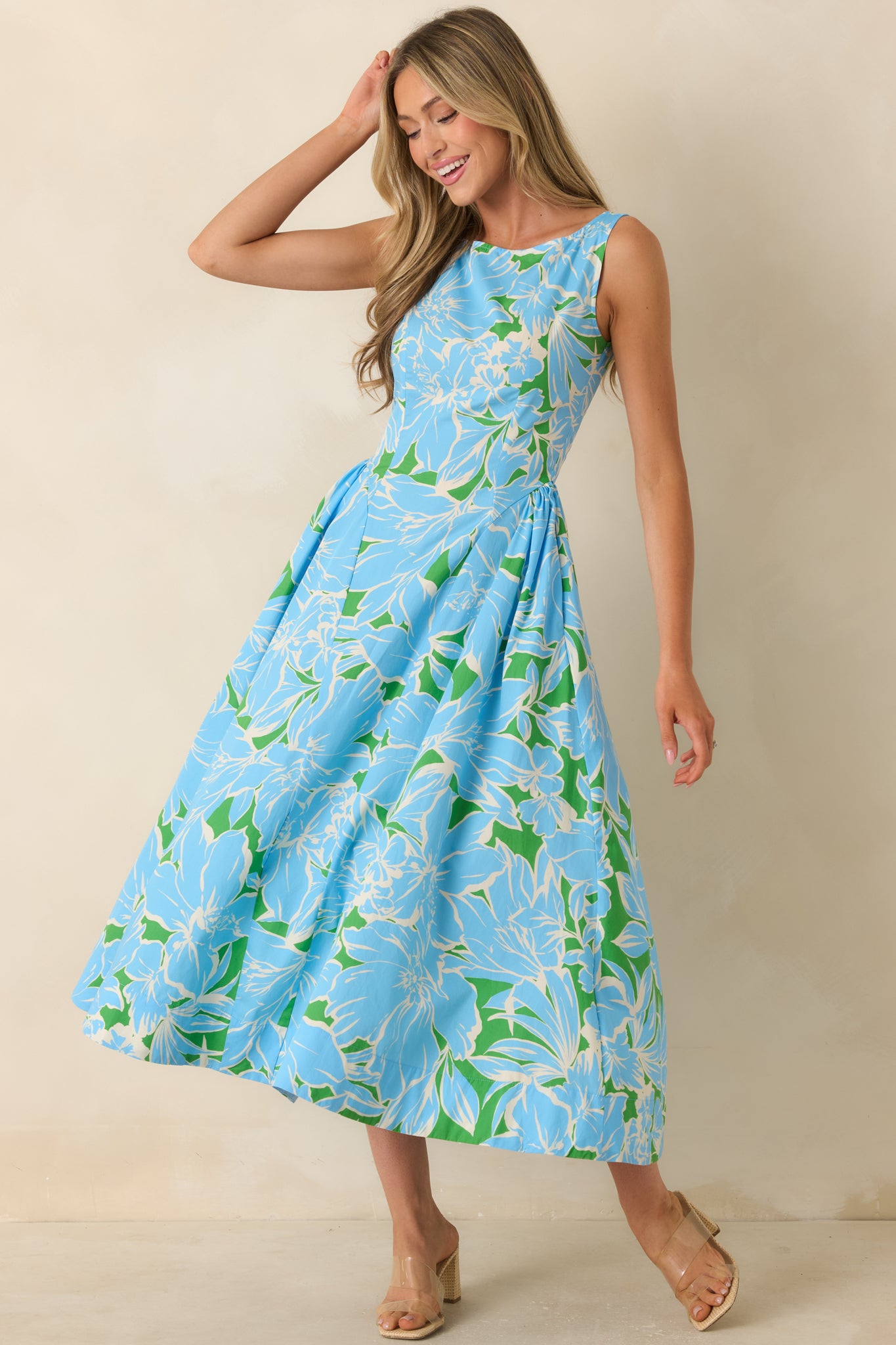 Blue and green floral cotton midi dress featuring a fitted bodice, sleeveless silhouette, hidden side pockets, and a full flowing skirt.