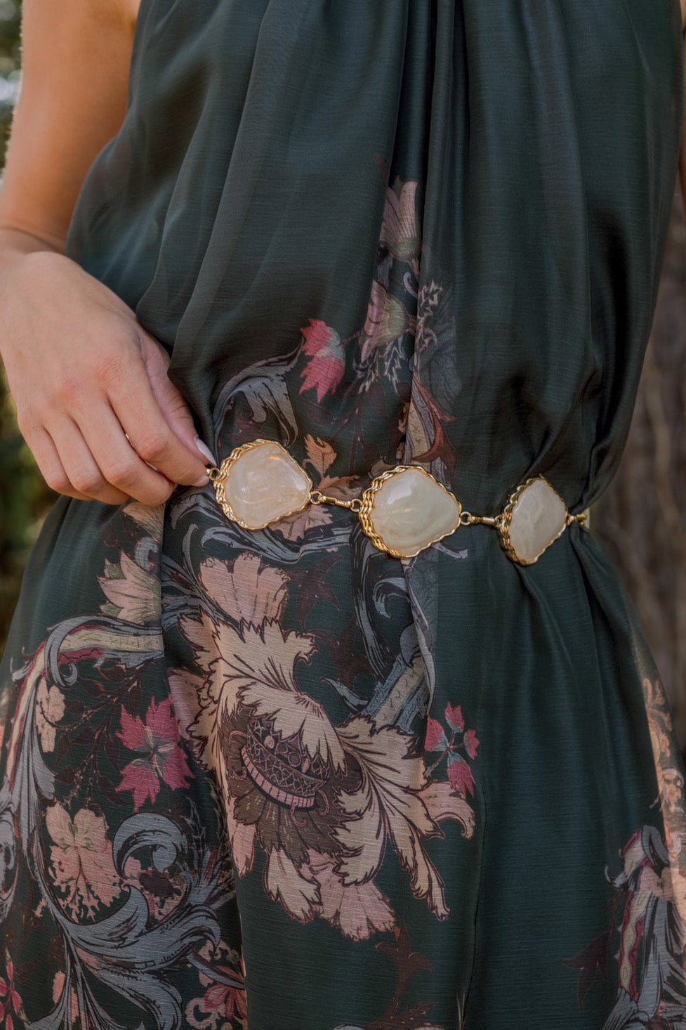 Close-up of a chain belt showing irregular stone-shaped embellishments and textured metal links in a dainty finish.