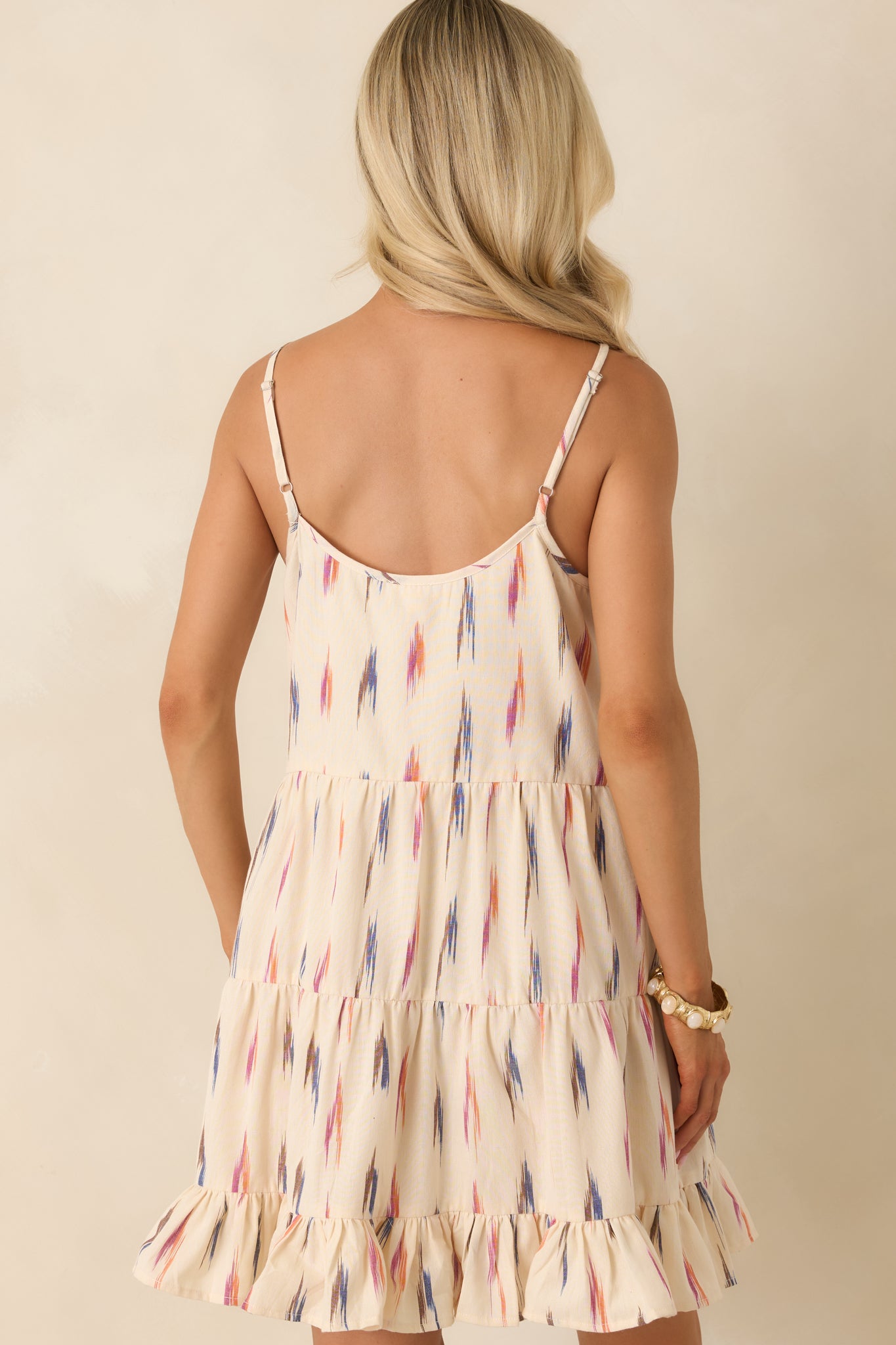 Rear view of the ivory multi print mini dress featuring adjustable spaghetti straps and a tiered silhouette with a ruffled hem.