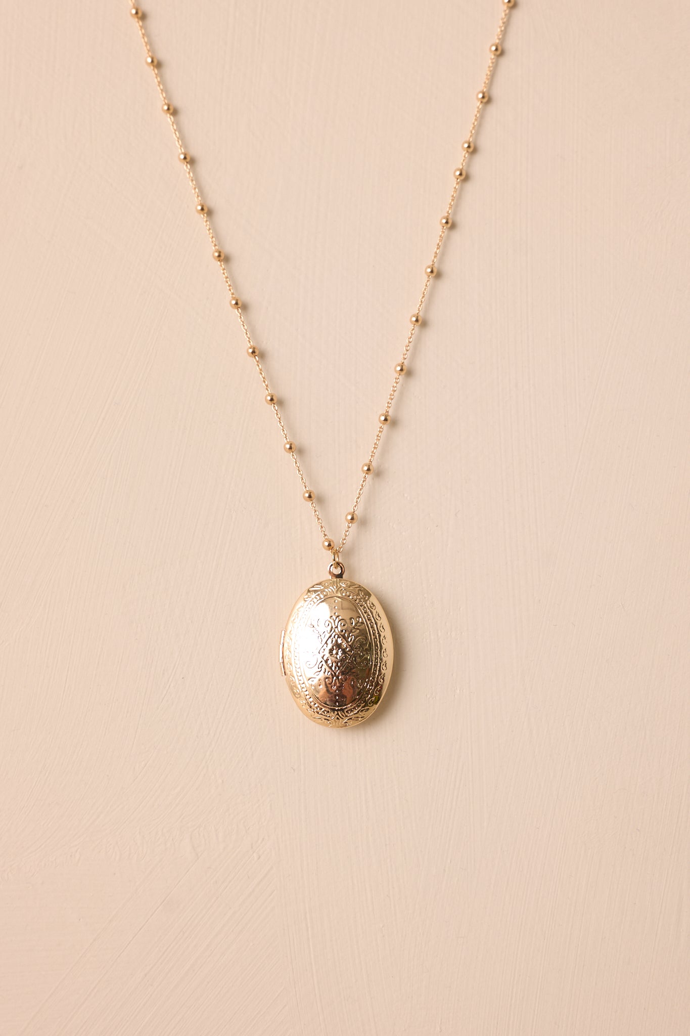 Close-up of the large gold oval locket, revealing the faint engraved pattern on both sides and the fine gold beading along the chain.
