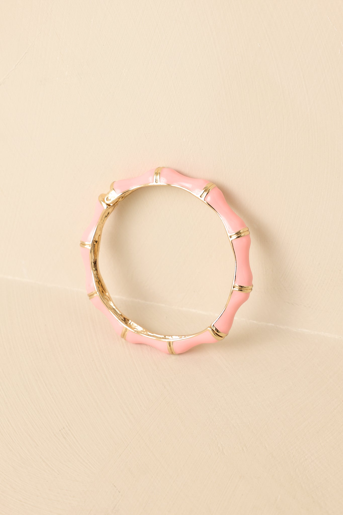Pink enamel bangle bracelet displayed on beige background, showing bamboo-inspired gold accents and sleek silhouette.