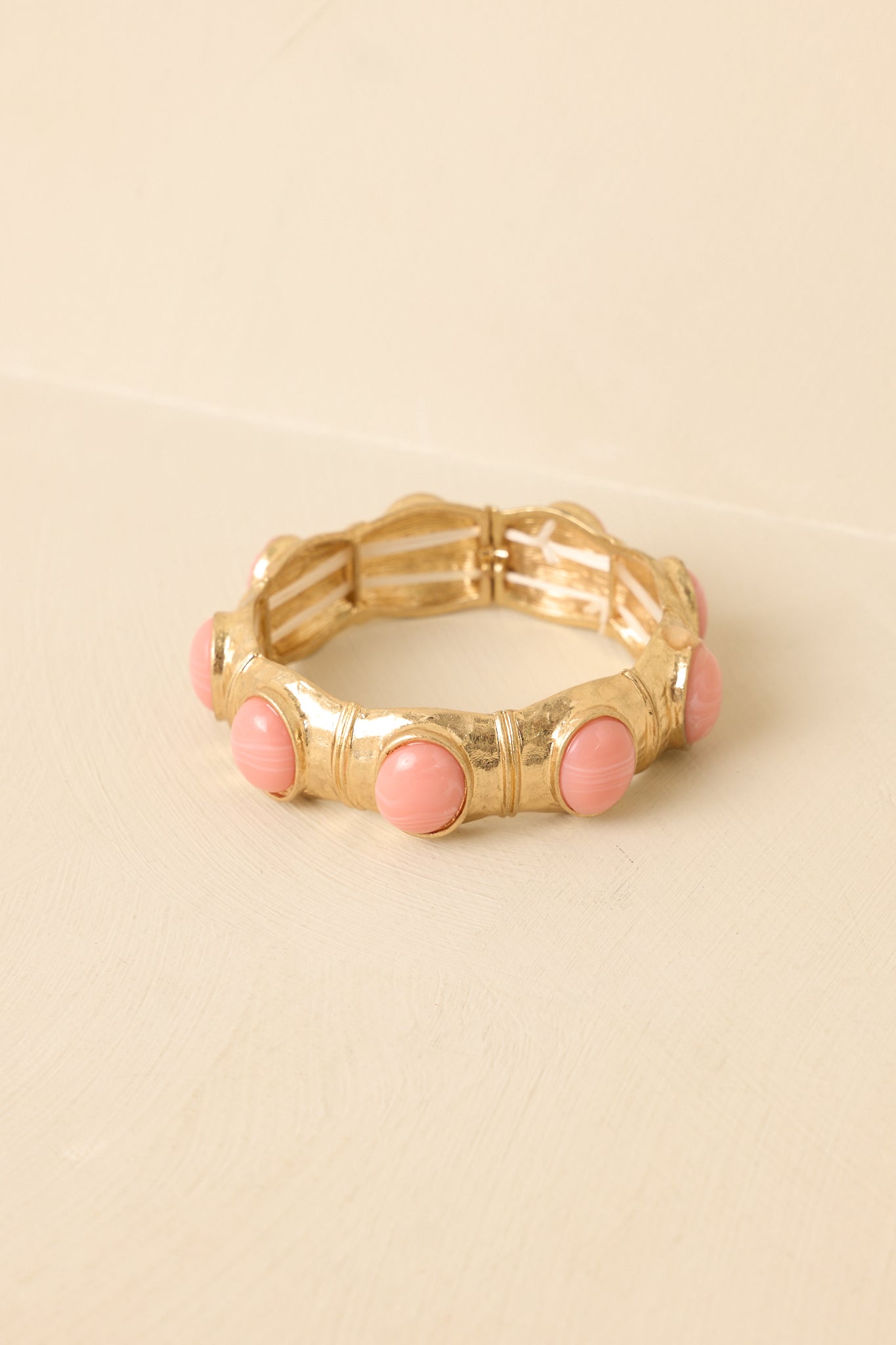 Close-up of gold-tone bracelet links framing smooth pink cabochons, highlighting the textured metalwork and glossy stone finish.