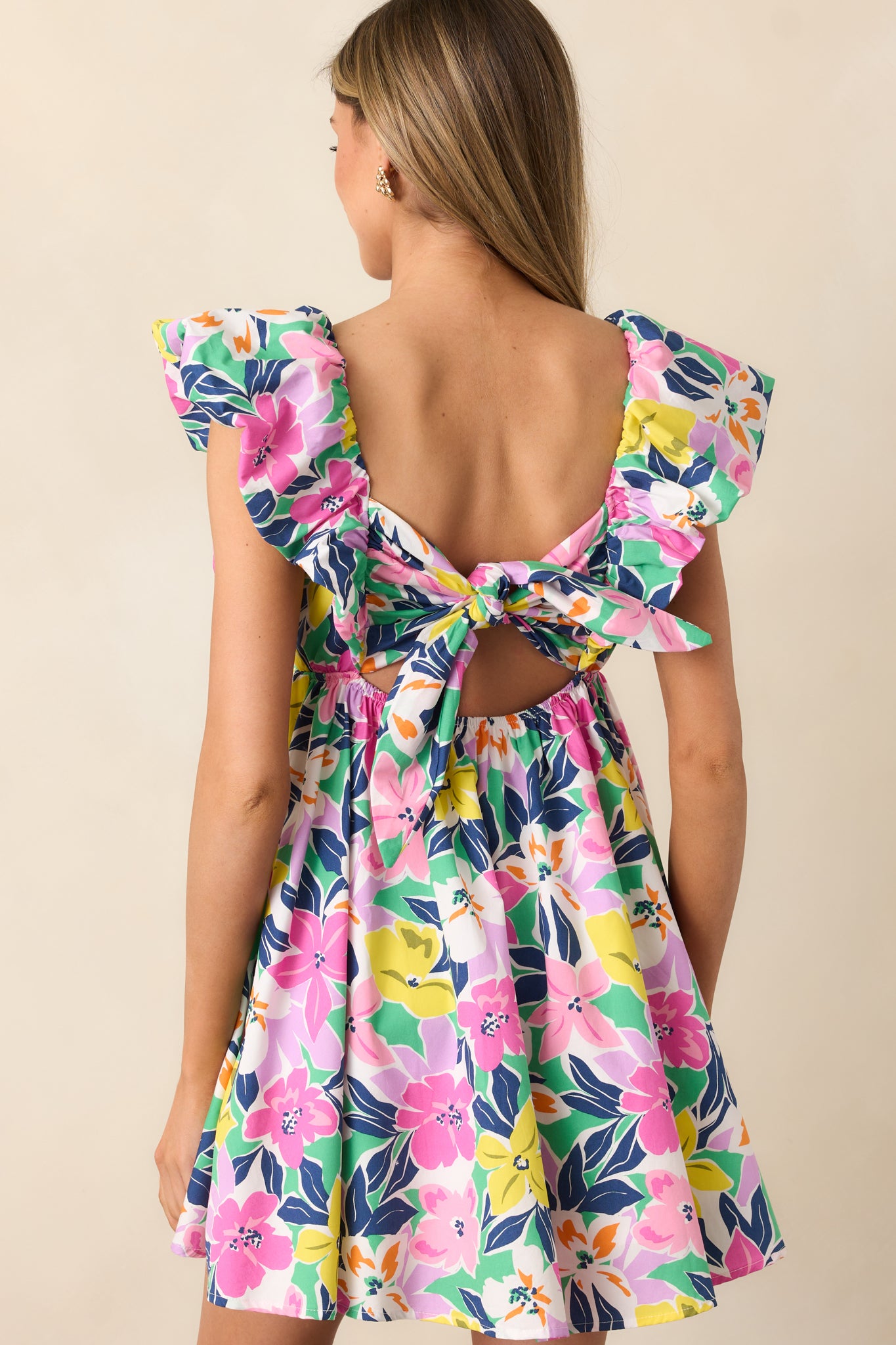 The back of the pink floral dress reveals the self-tie feature and elastic waistband, while the flutter sleeves and babydoll cut create a flattering, feminine silhouette