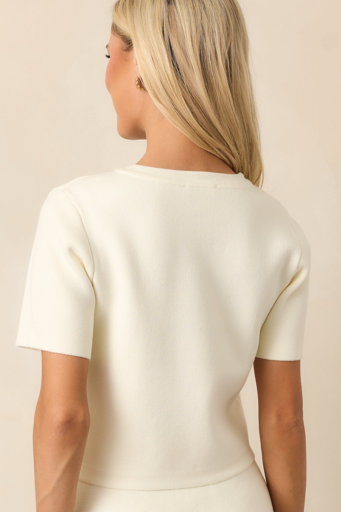 The back view of the ivory cardigan, highlighting its cropped length and simple, clean lines, with no extra embellishments to maintain a sleek, elegant style.