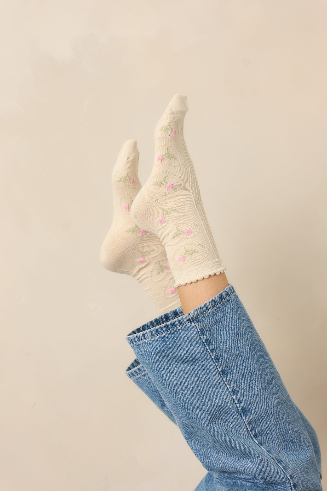 A side view of the beige crew socks, highlighting the small woven hearts with roses inside along the sides.