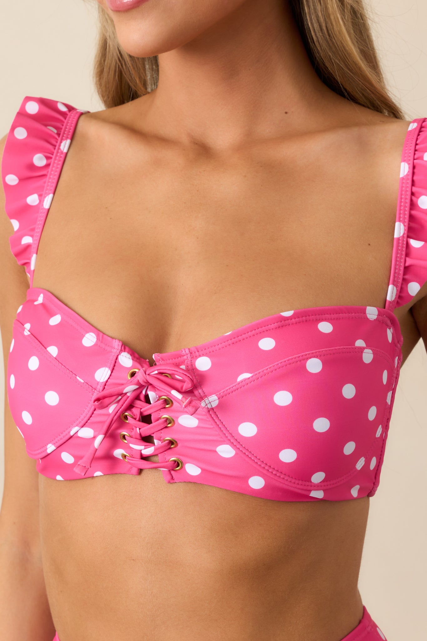 A detailed shot of the pink bikini top with white polka dots, showcasing the lace-up front closure, adjustable straps with ruffled edges, and removable padding.