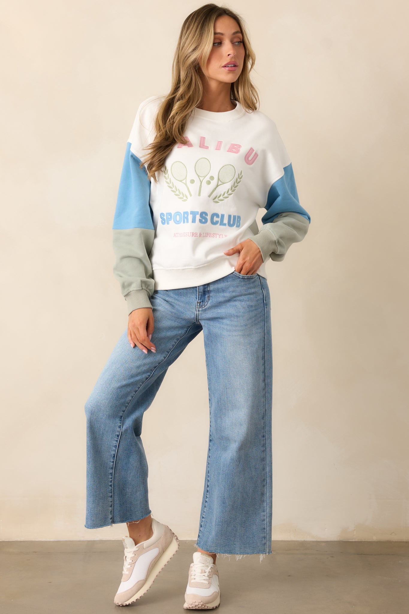 A cozy white sweatshirt with colorblocked sleeves and a bold "Malibu Sports Club" graphic, perfect for casual, sporty style.