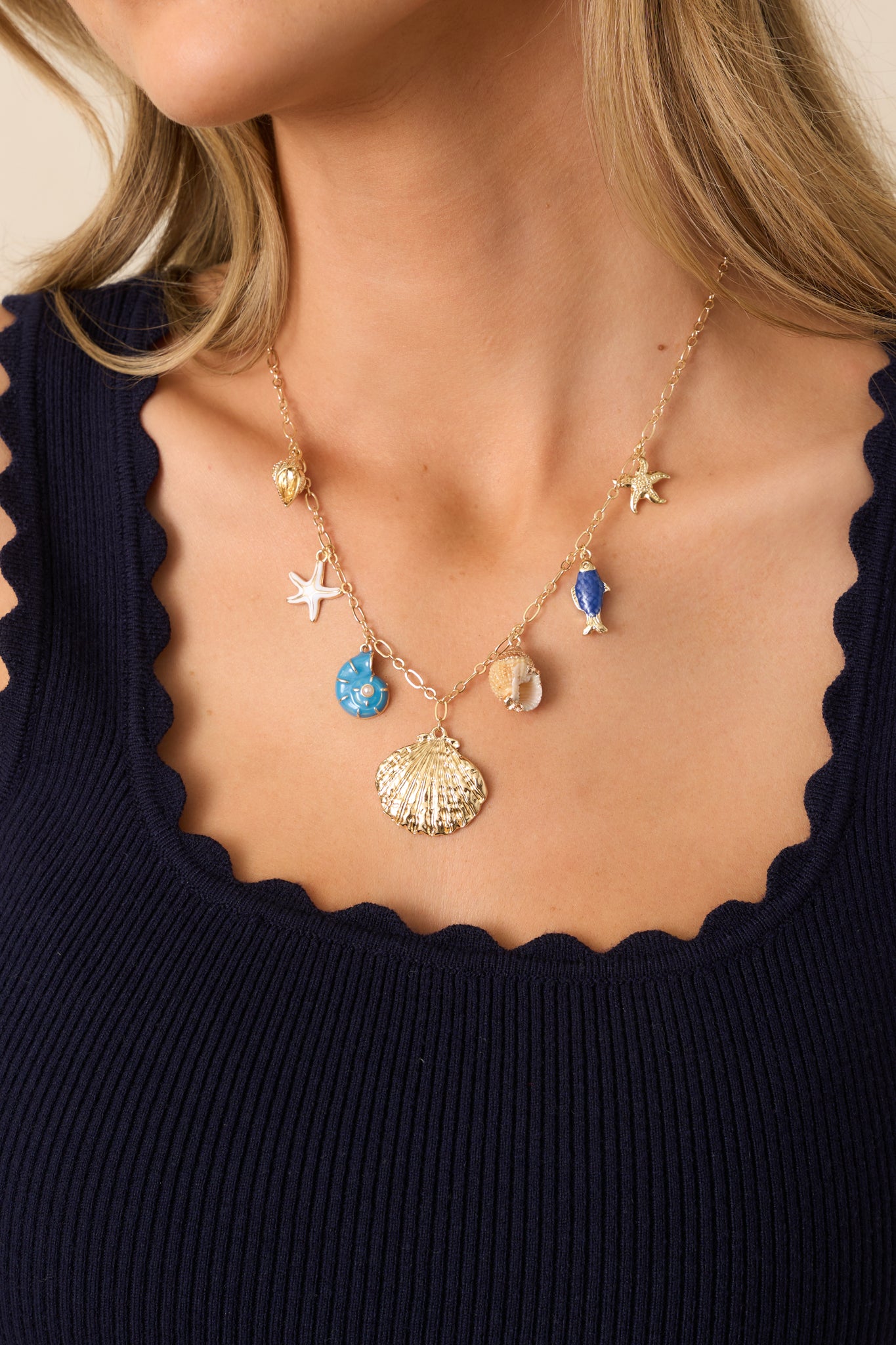 A gold charm necklace with a thin gold chain, featuring a variety of gold, white, and blue seashell pendants connected by gold jump rings.