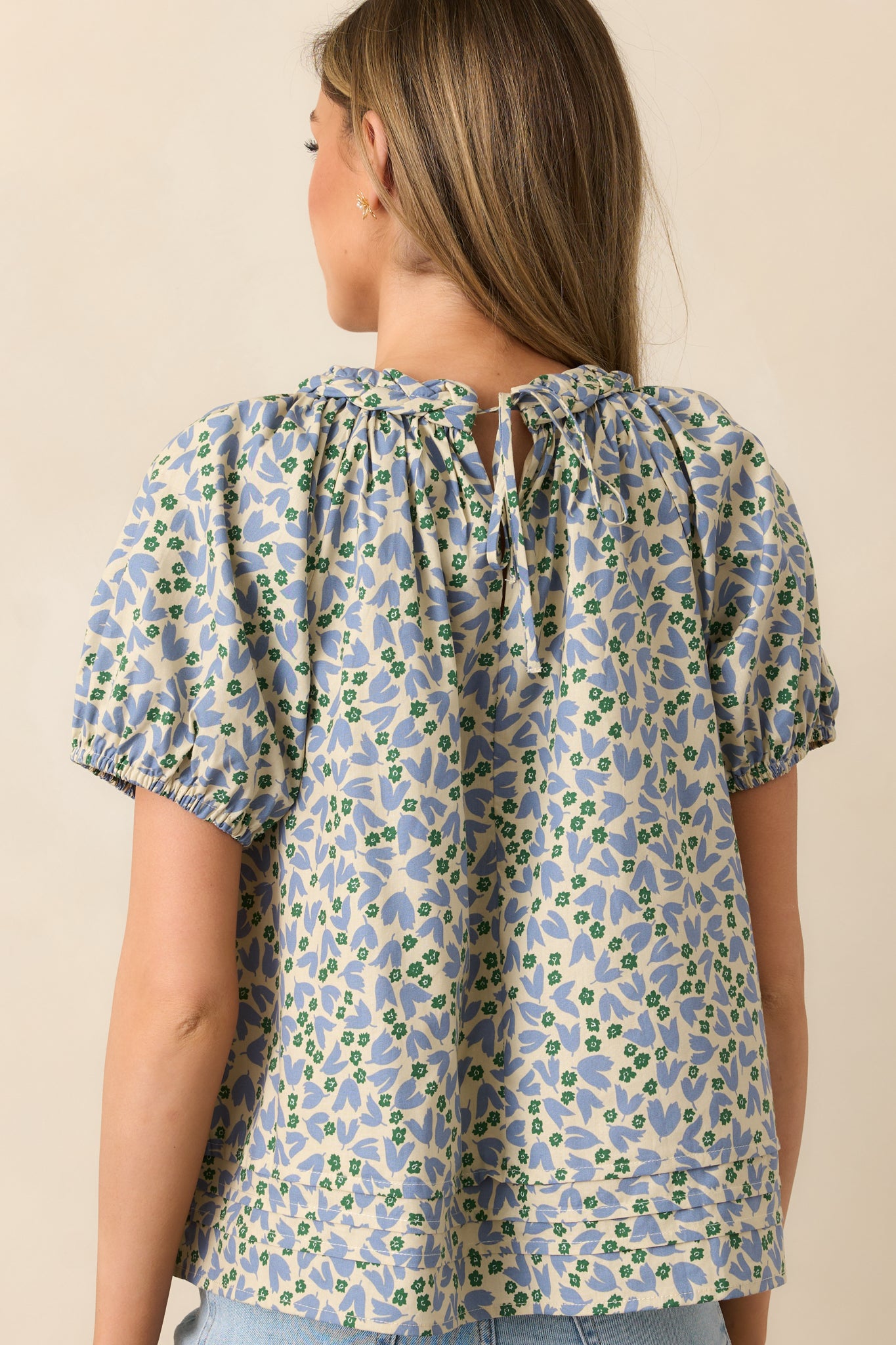 A view from behind of the dusty blue blouse, featuring the self-tie keyhole closure and relaxed drape.