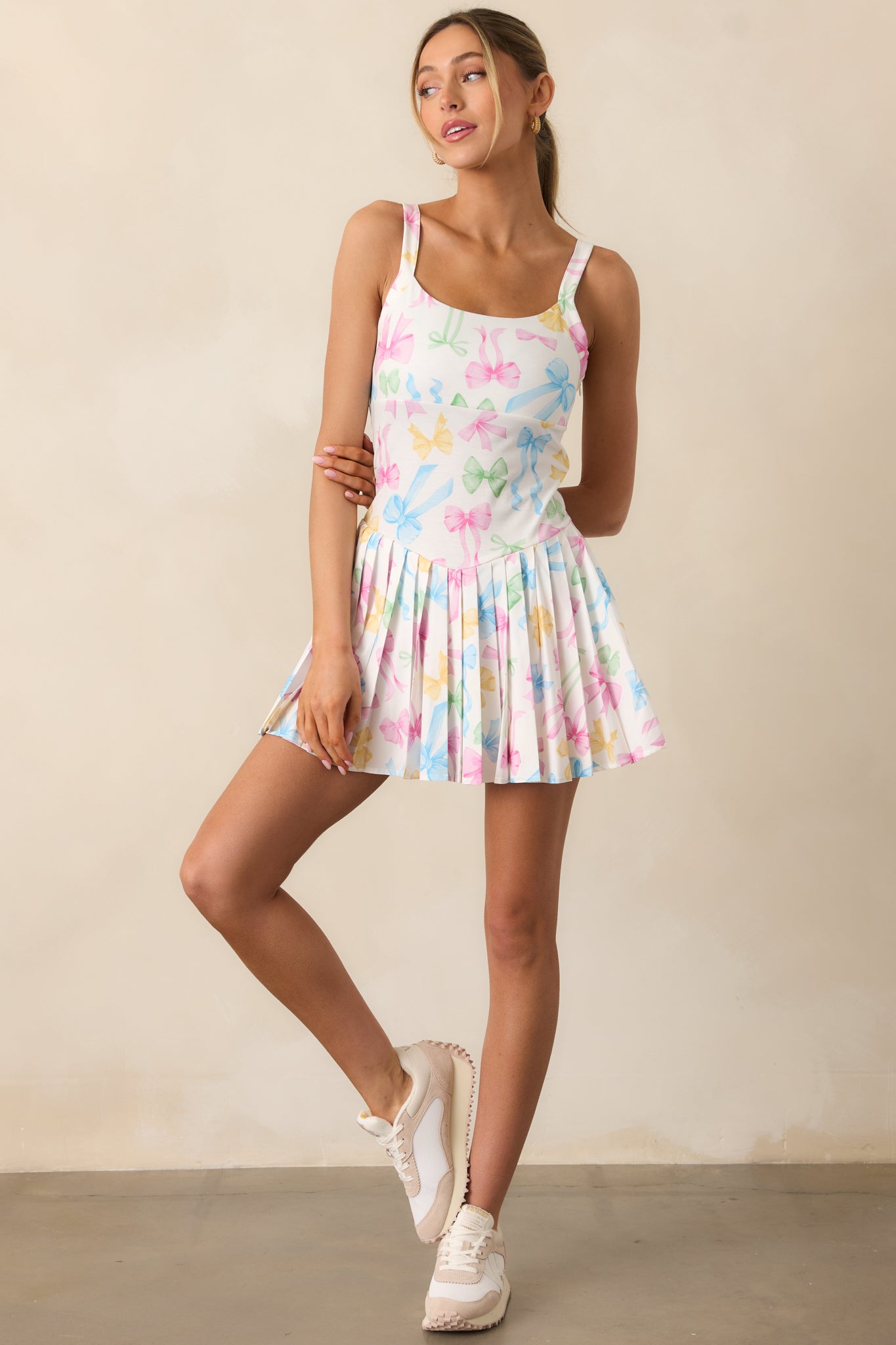The pastel mini dress showcases a square neckline, thin straps, and a pleated skirt with built-in shorts, all highlighted by a sweet pastel bow design.