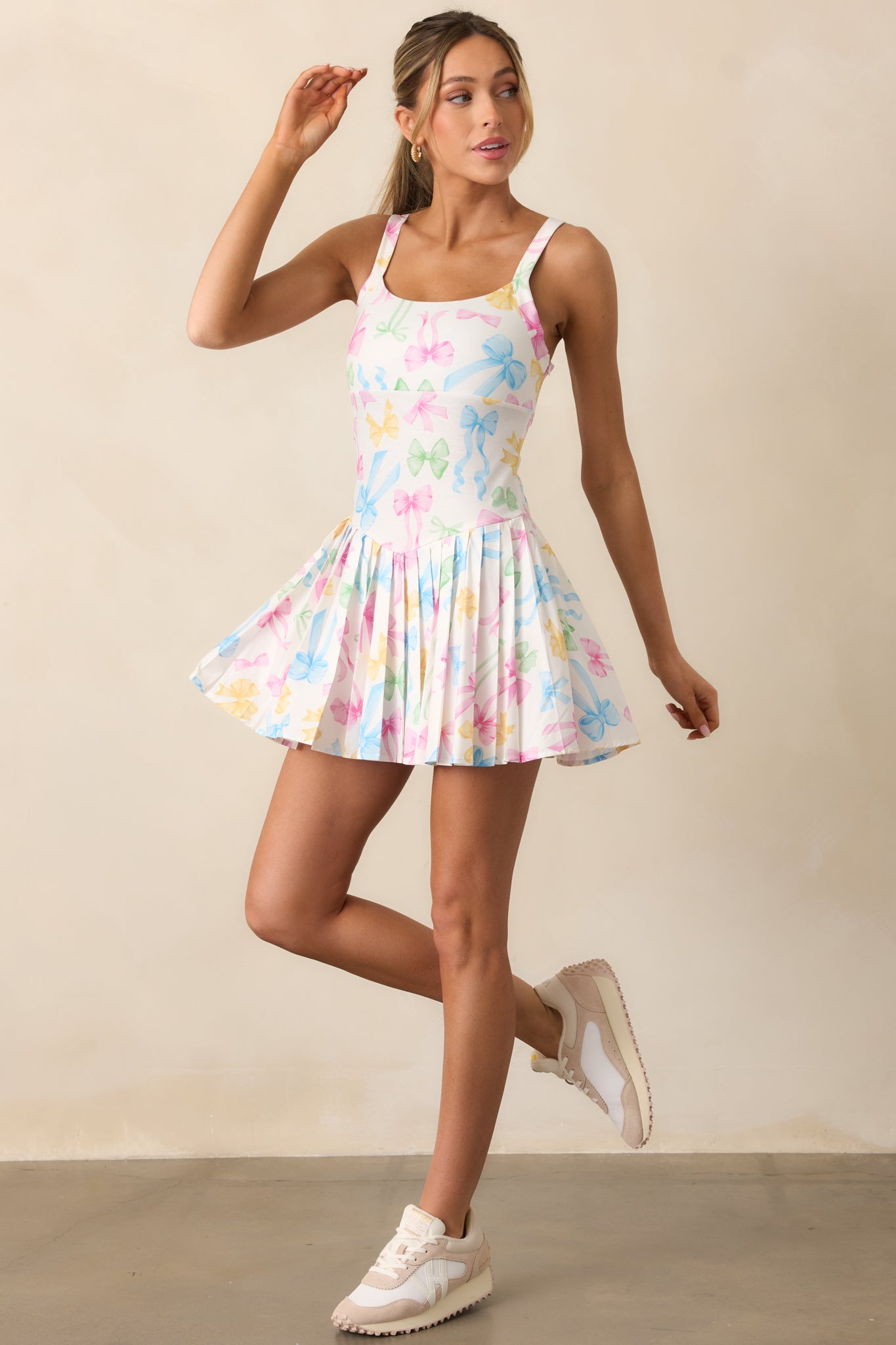 This pastel mini dress features a square neckline, thin straps, and a pleated skirt with built-in shorts underneath, adorned with a playful pastel bow pattern.