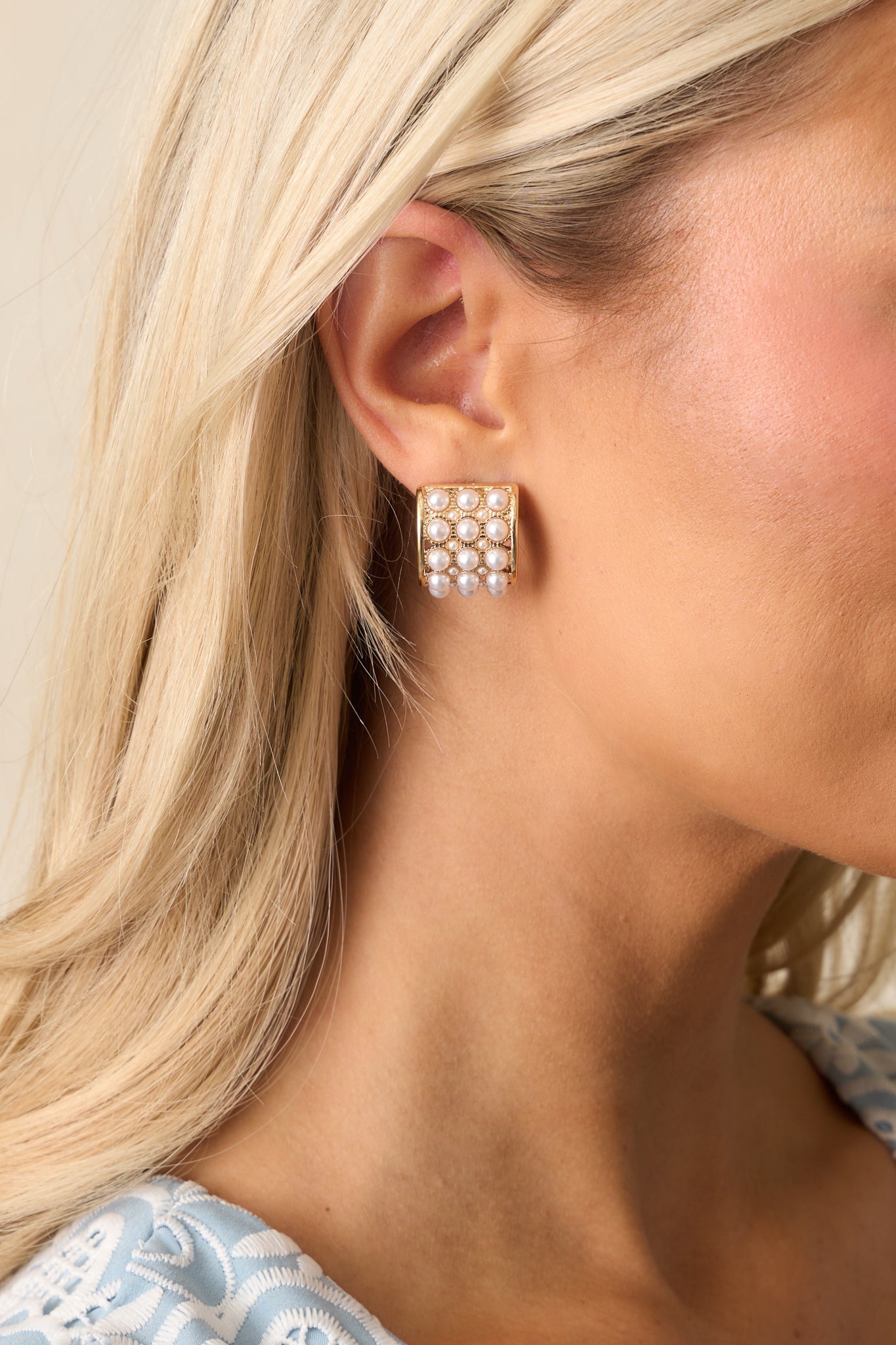 A pair of gold and ivory earrings featuring gold hardware, a c-hoop design, and solid gold rectangular shapes with medium-sized faux ivory pearls bordered by textured gold.