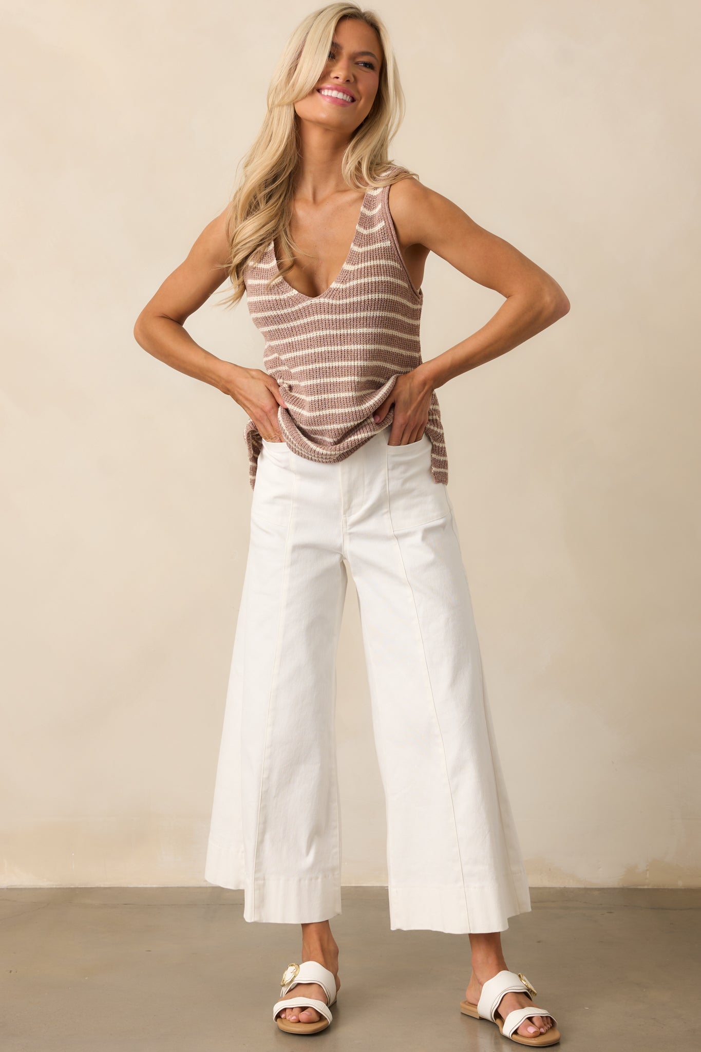 Full length view of white pants with a high waisted design, a double button closure with a zipper, functional front pockets, front & back seams, and a wide leg with a cropped length.